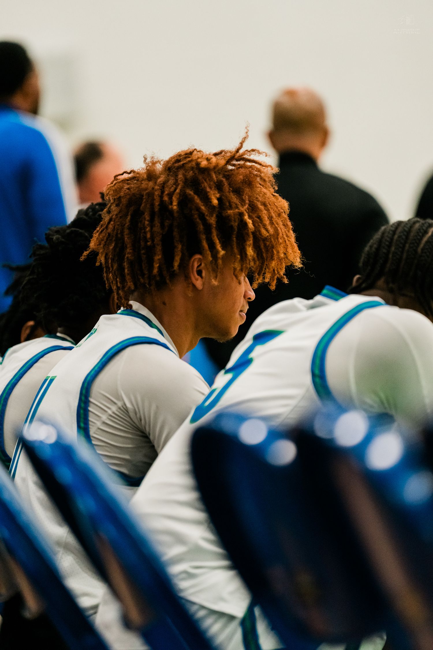 Basketball player with red dreadlocks sits on bench in white and blue uniform.