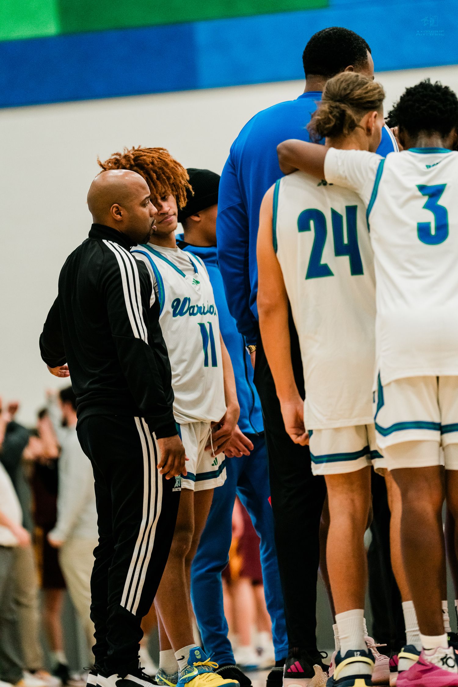 Coach and Warriors basketball player #11 stand on the sideline while players #24 and #3 huddle nearby.