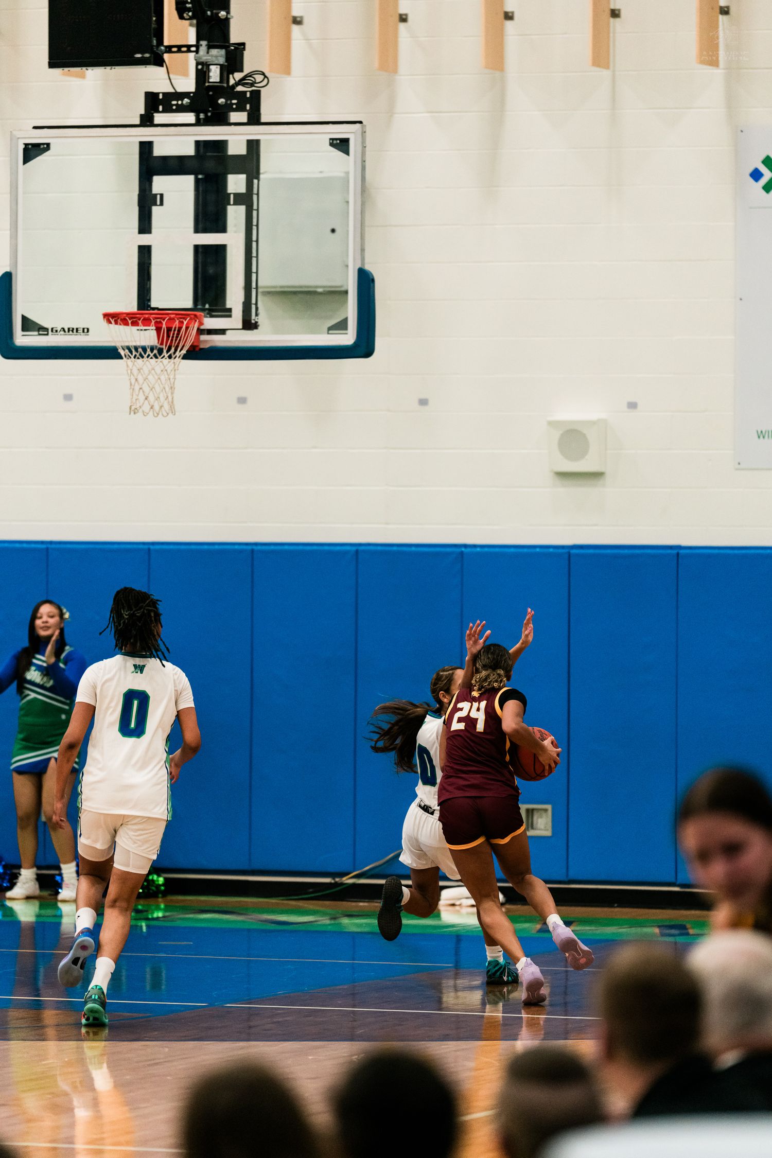 A maroon-uniformed player number 24 drives toward the basket while a defender contests the shot in girls basketball.
