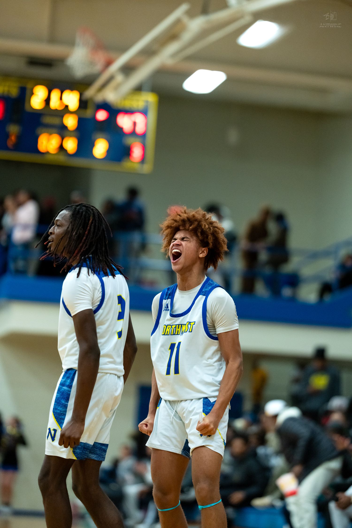 Two high school basketball players in white uniforms celebrate excitedly during a home game.