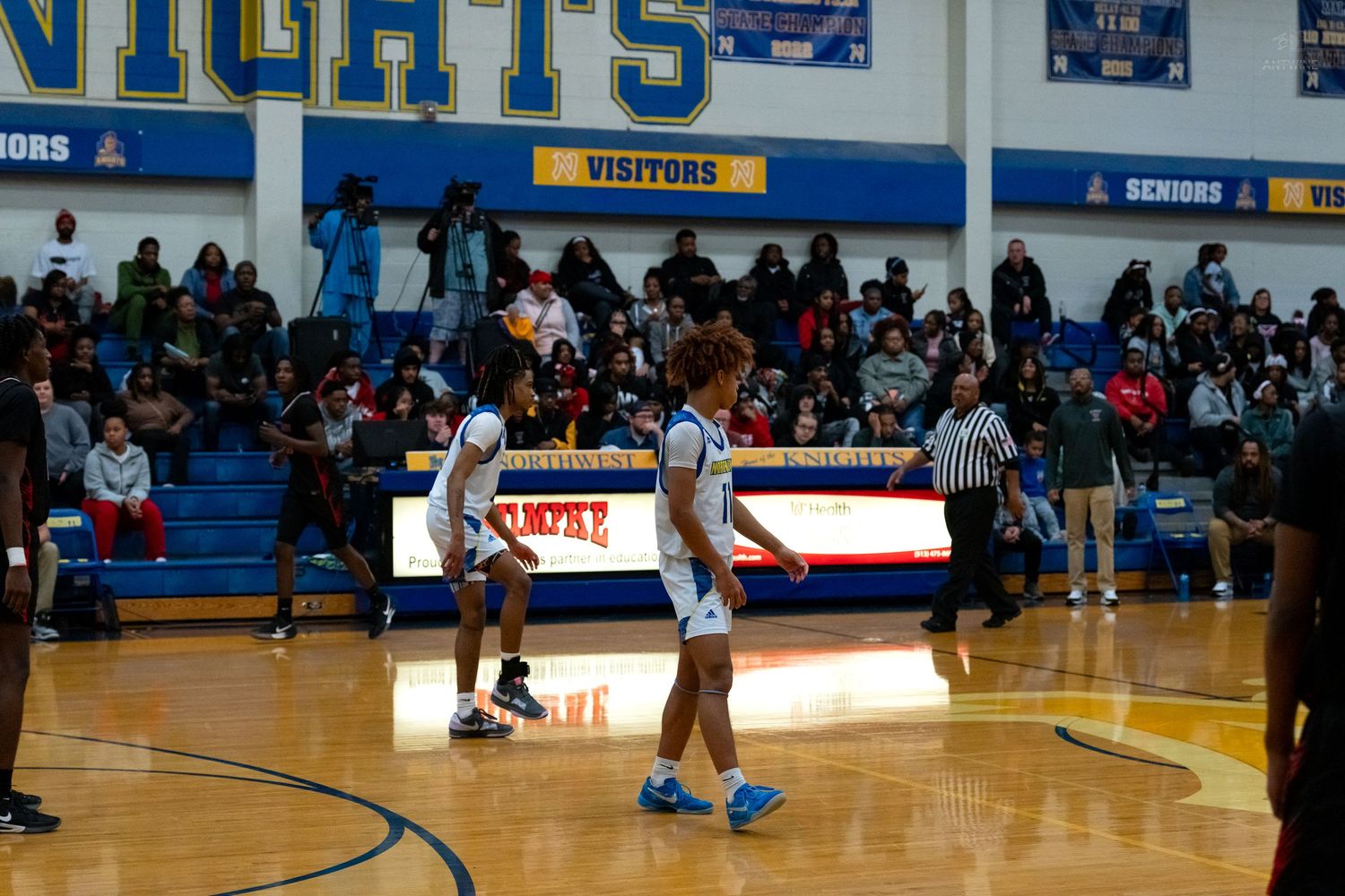 Two high school basketball players in blue uniforms walk across court during a game.