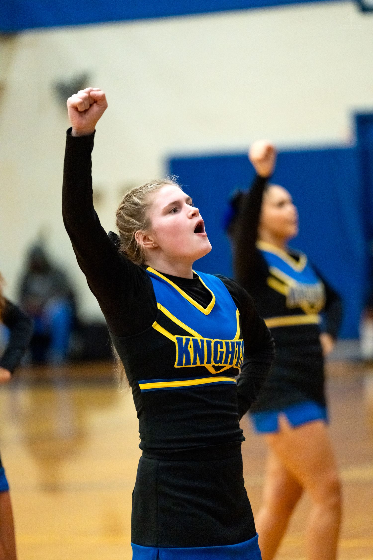 Energetic Knights cheerleader raises fist while cheering during high school basketball game.