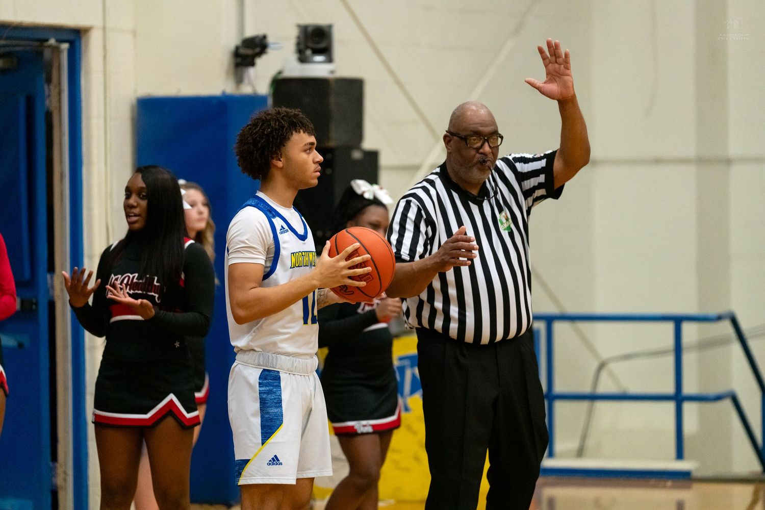 A referee signals while a high school basketball player prepares for an inbound pass.