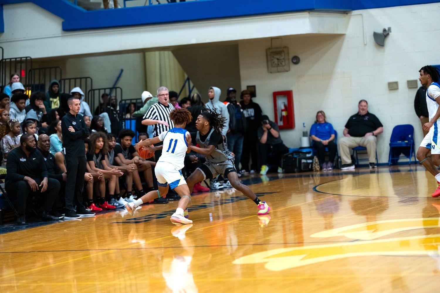 Basketball player wearing number 11 dribbles past defender during indoor high school basketball game.