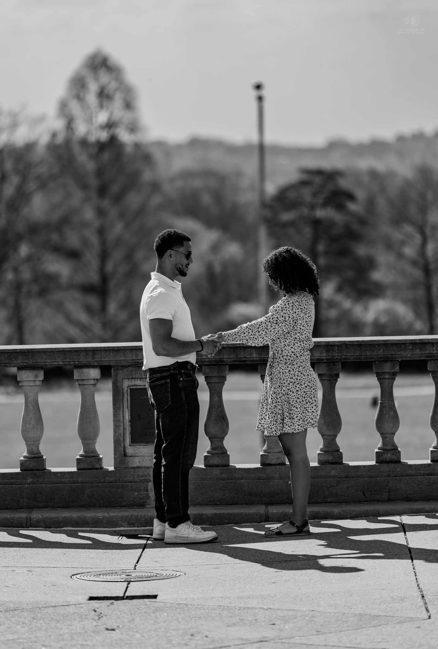 Black and white image of a couple holding hands on an ornate stone balcony in a park.