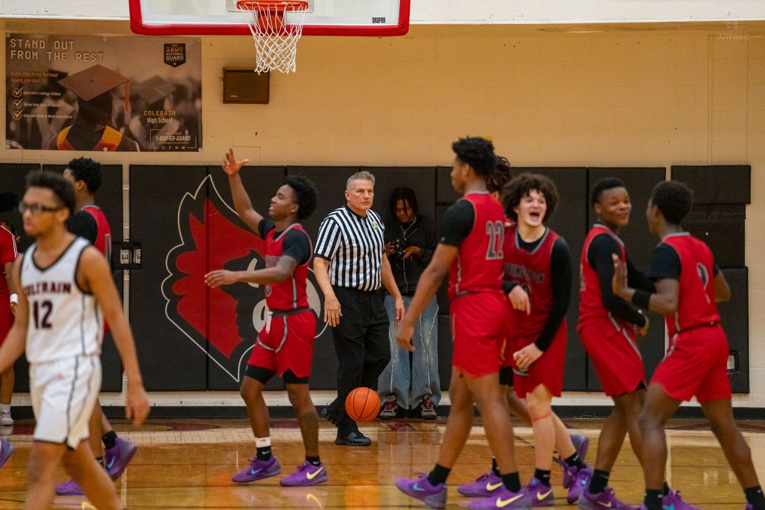 A referee signals a call as basketball players in red and white react during a high school game.