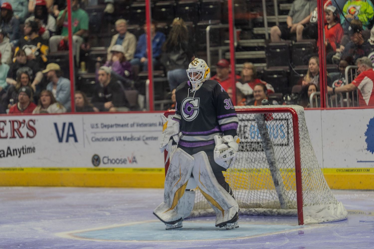 Hockey goalie in colorful mask guards the net during a professional ice hockey game.