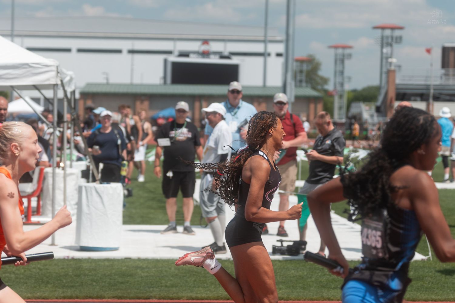 Female sprinters crossing finish line at outdoor track and field championship meet with spectators watching.