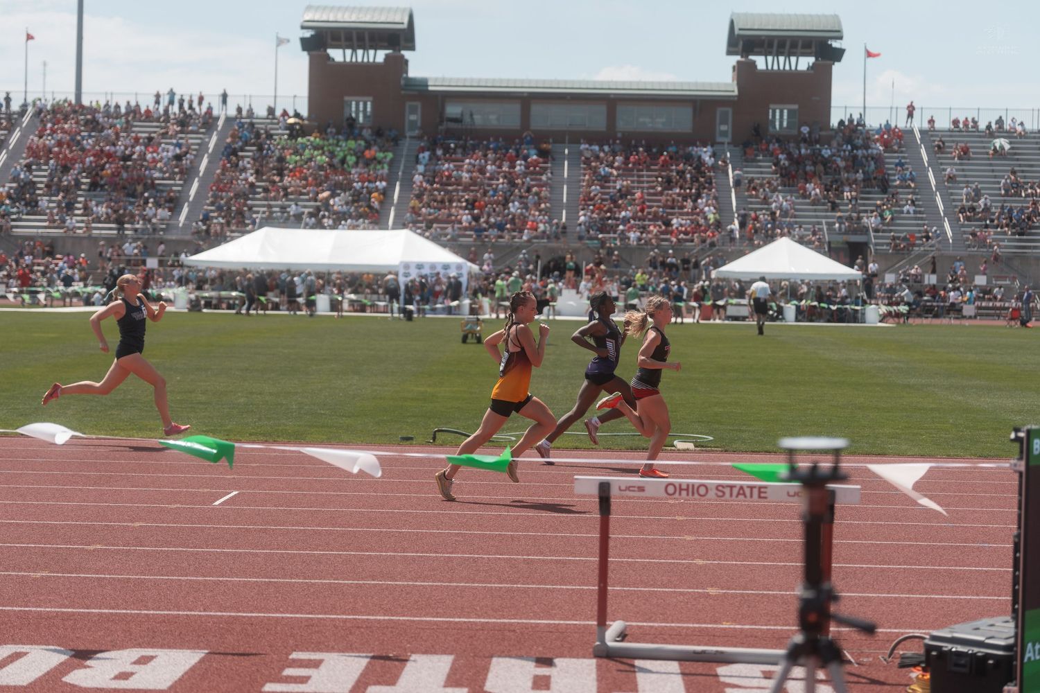 Female sprinters race toward the finish at a crowded Ohio State University track and field event.