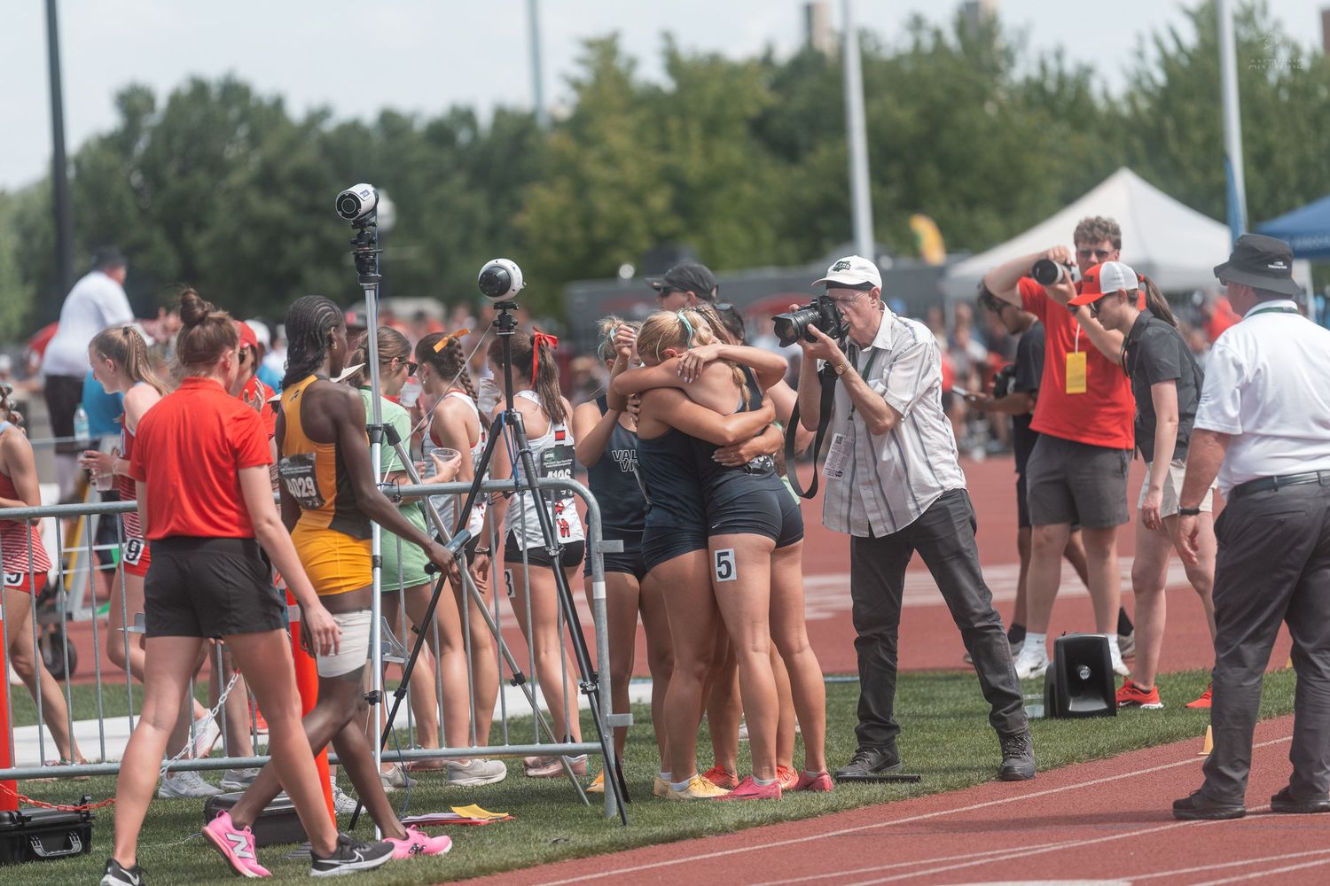 Female track athletes celebrating together on the track surrounded by spectators and photographers.