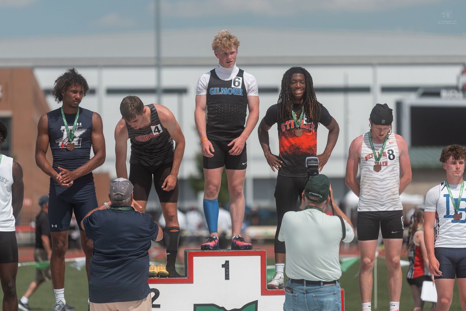 Male high school athletes stand on numbered award podium at OHSAA track and field championship.