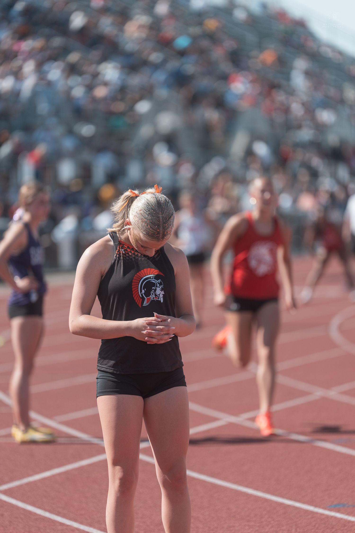 A female track athlete in a Trojan uniform checks her phone on the red track after a race at a large meet.