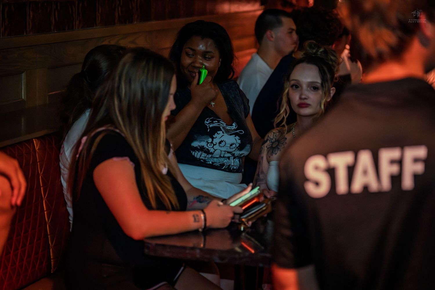Group of friends relax at a bar booth with staff member nearby.