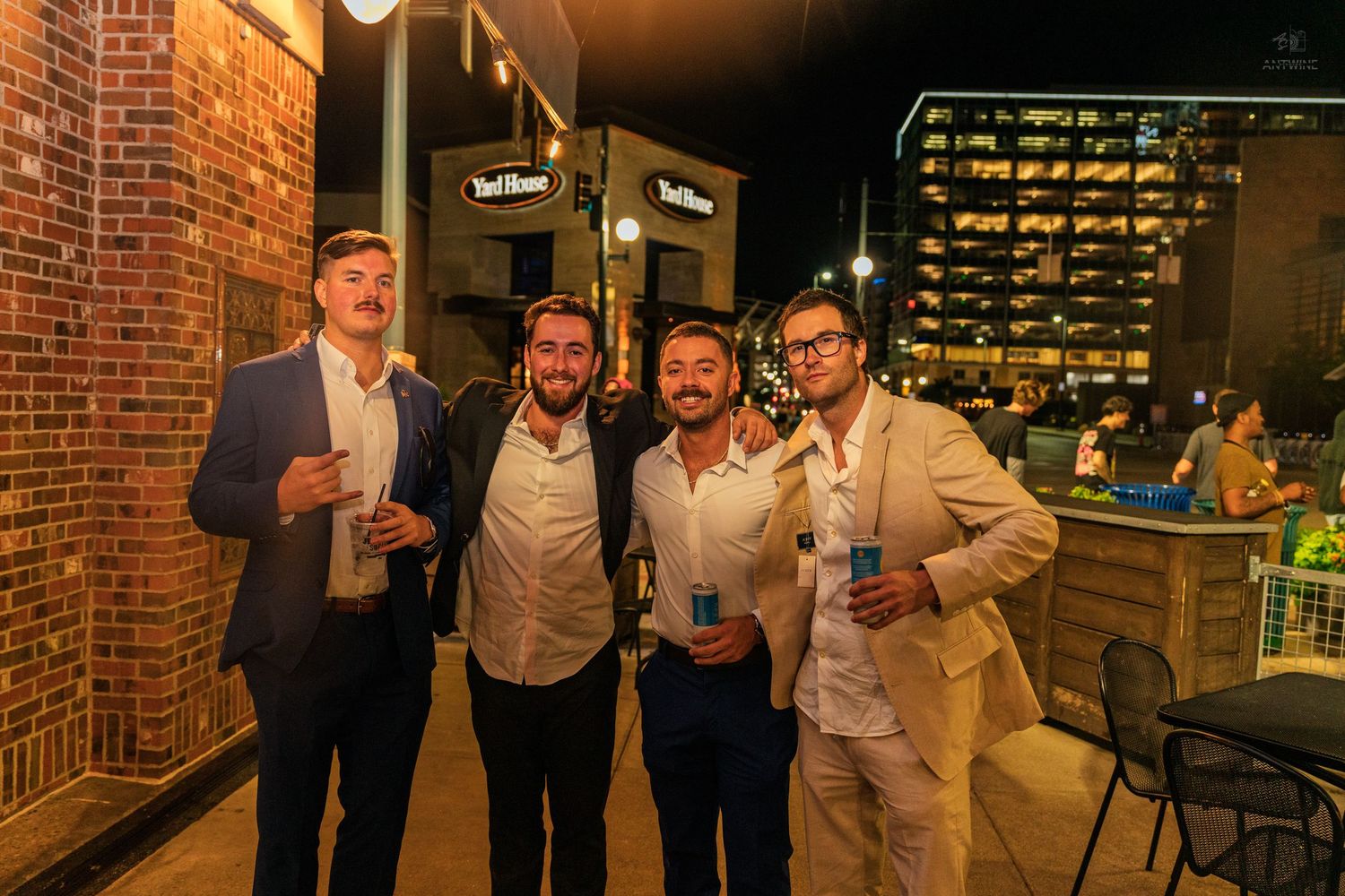 Four men in smart casual attire posing together outside a bar at night.