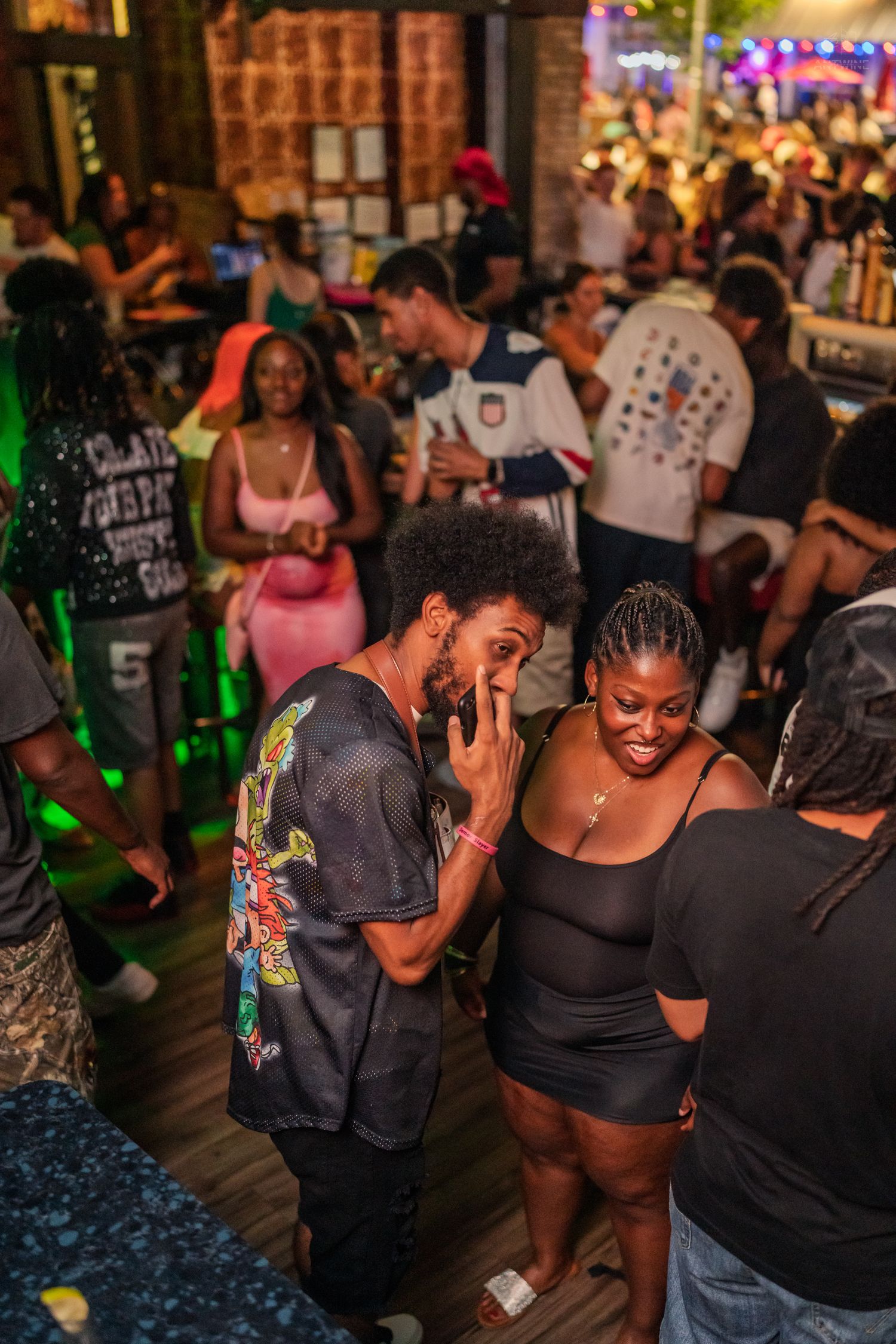Two people laughing and chatting together on a busy nightclub dance floor with green lighting.