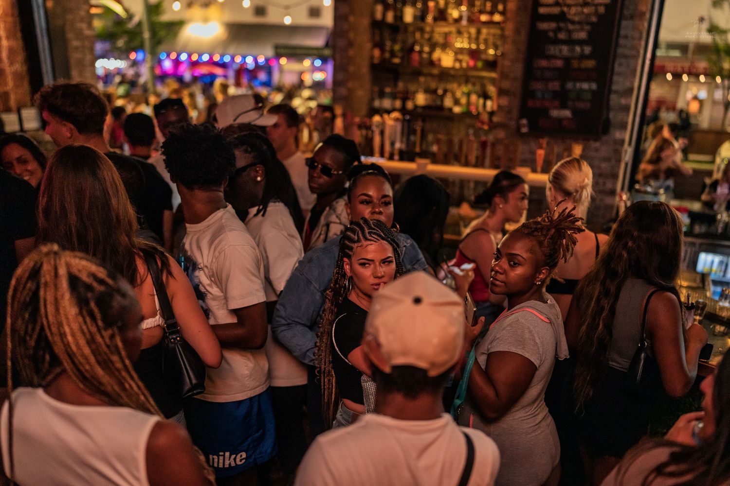 Lively nightclub scene with diverse group of people socializing near a well-stocked bar.