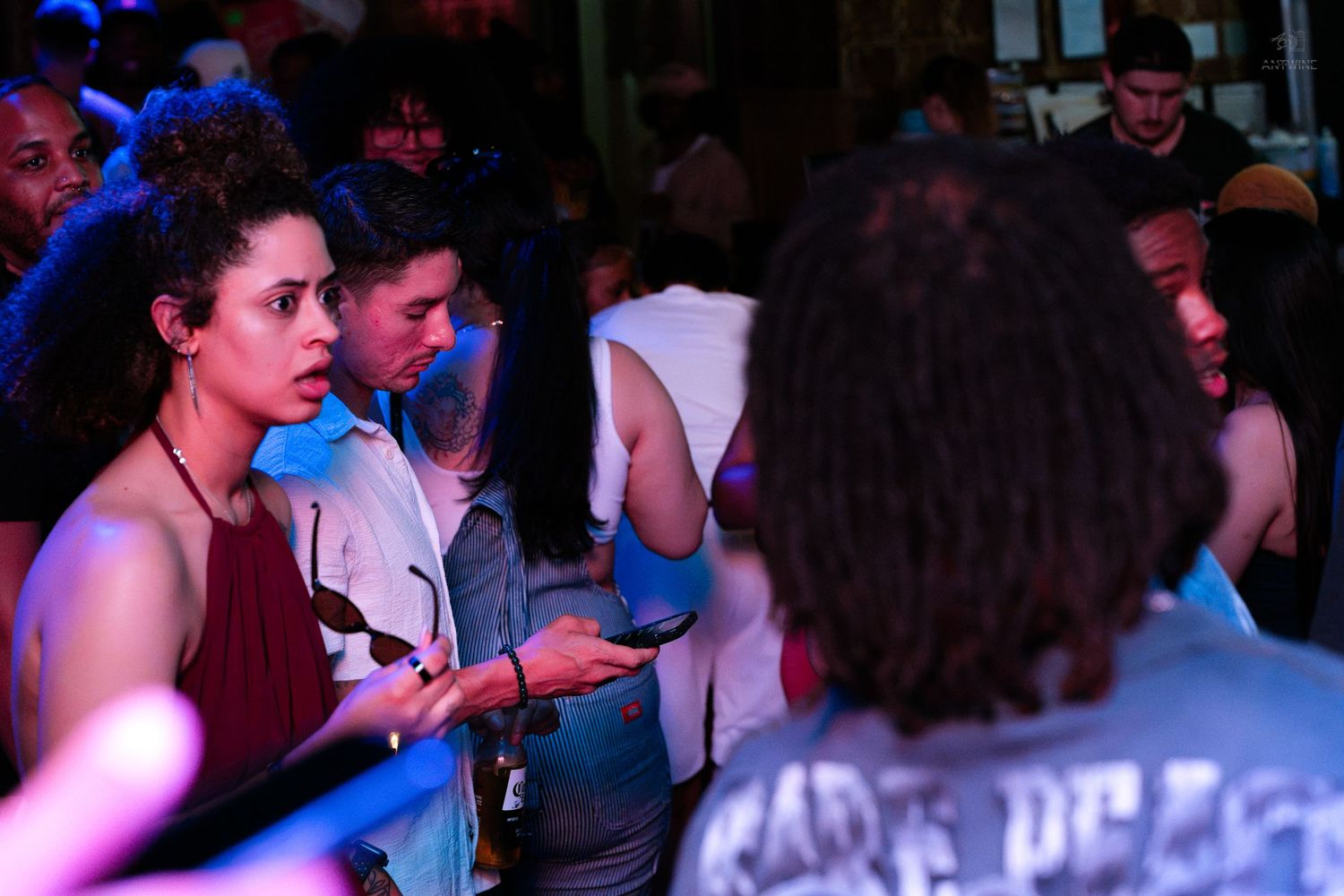 Woman holding phone talking to someone at a lively nightclub with blue lighting.