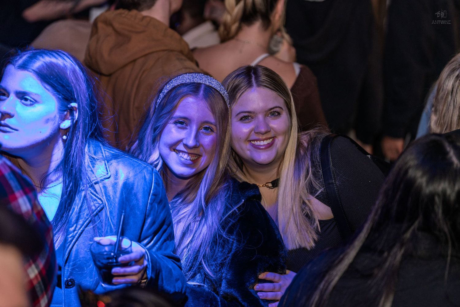 Two smiling young women pose together at a lively nightclub event under blue lights.
