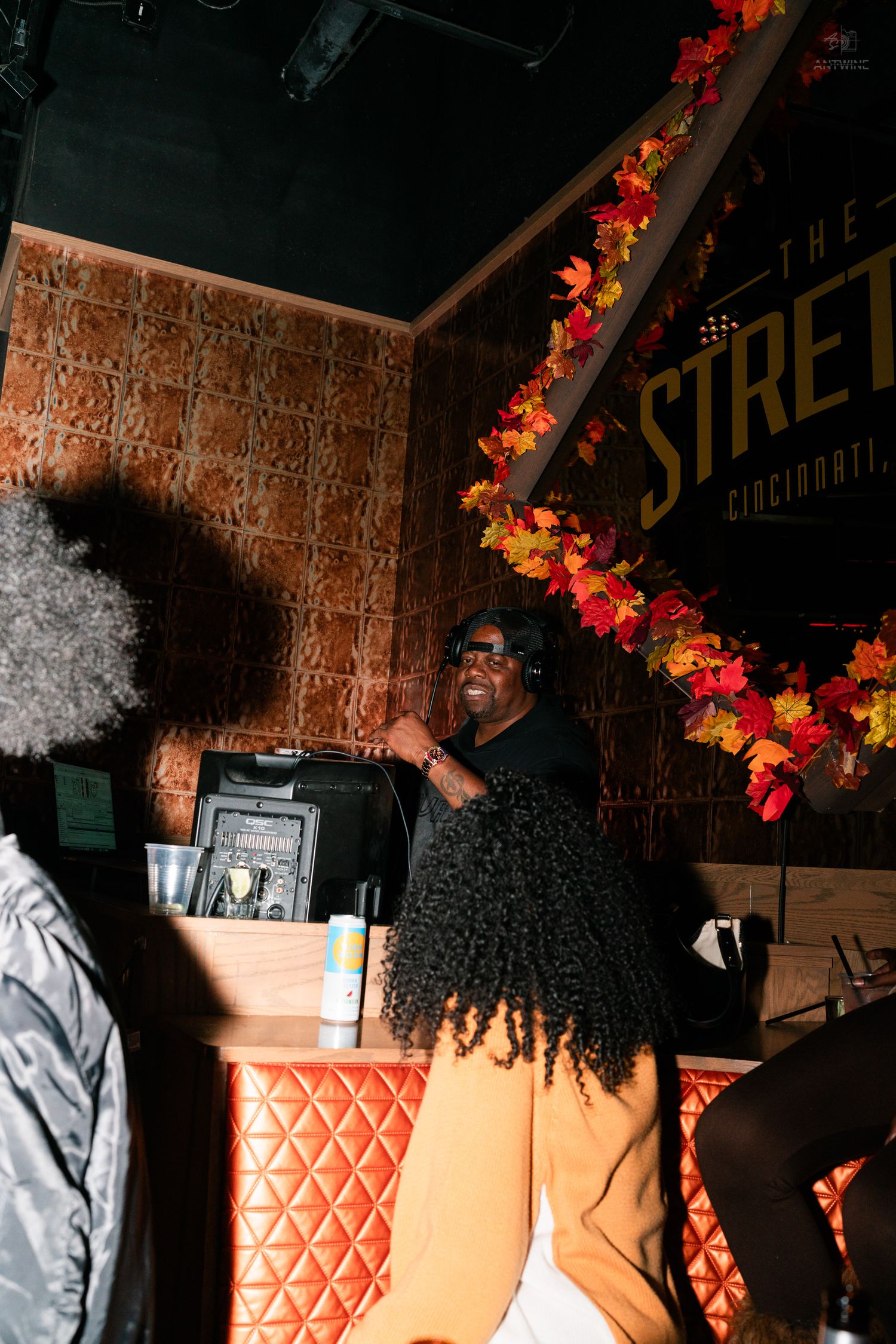 Woman with long curly hair smiling at a DJ booth decorated with fall leaves at The Street Cincinnati.
