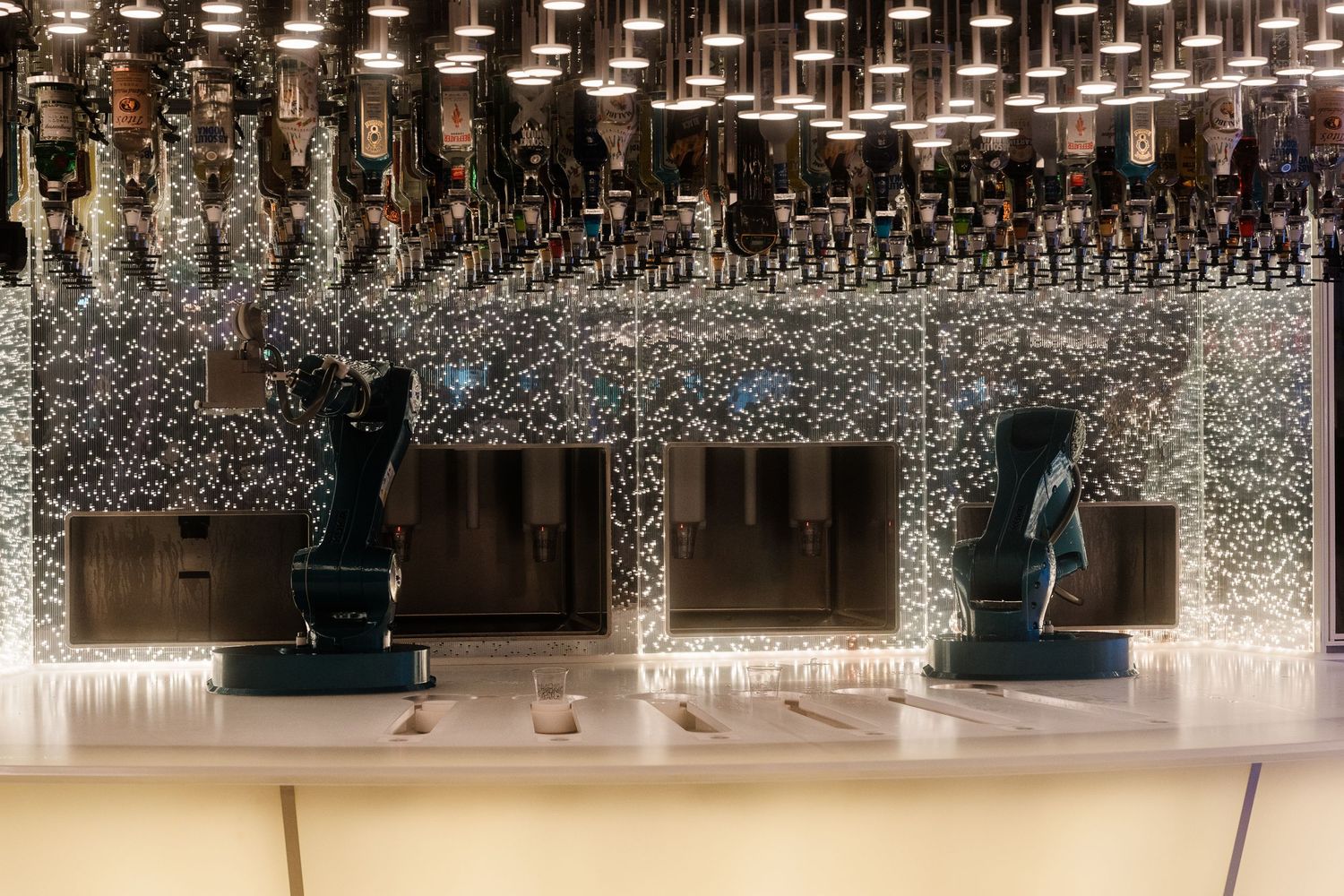Elegant cruise ship bar with sparkling mosaic backdrop, hanging lights, and decorative blue sculptures.