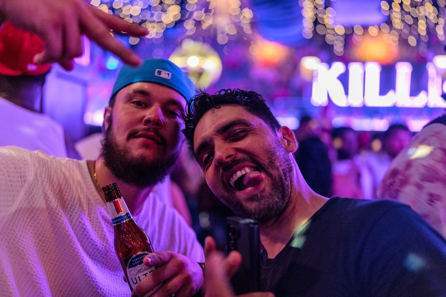 Two smiling men posing together at a vibrant nightclub with colorful lights.