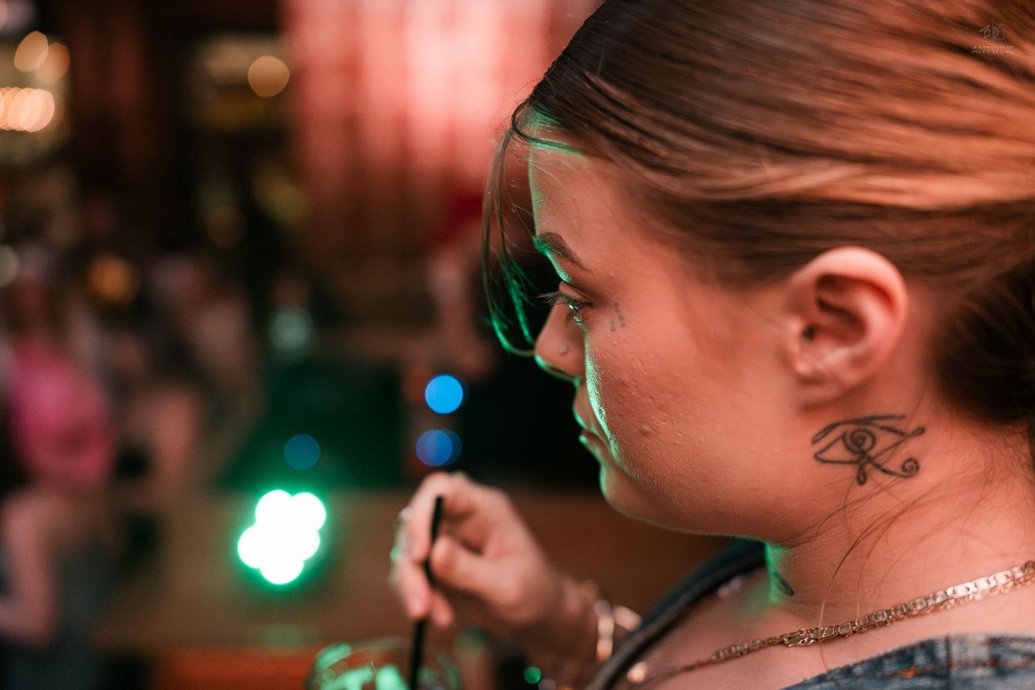 Close-up profile of a woman with an Eye of Ra neck tattoo in a nightclub setting.