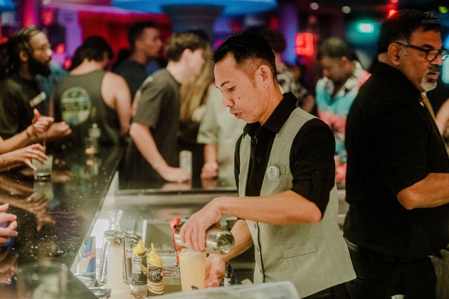 A bartender carefully prepares cocktails at a busy bar during a nightlife event.