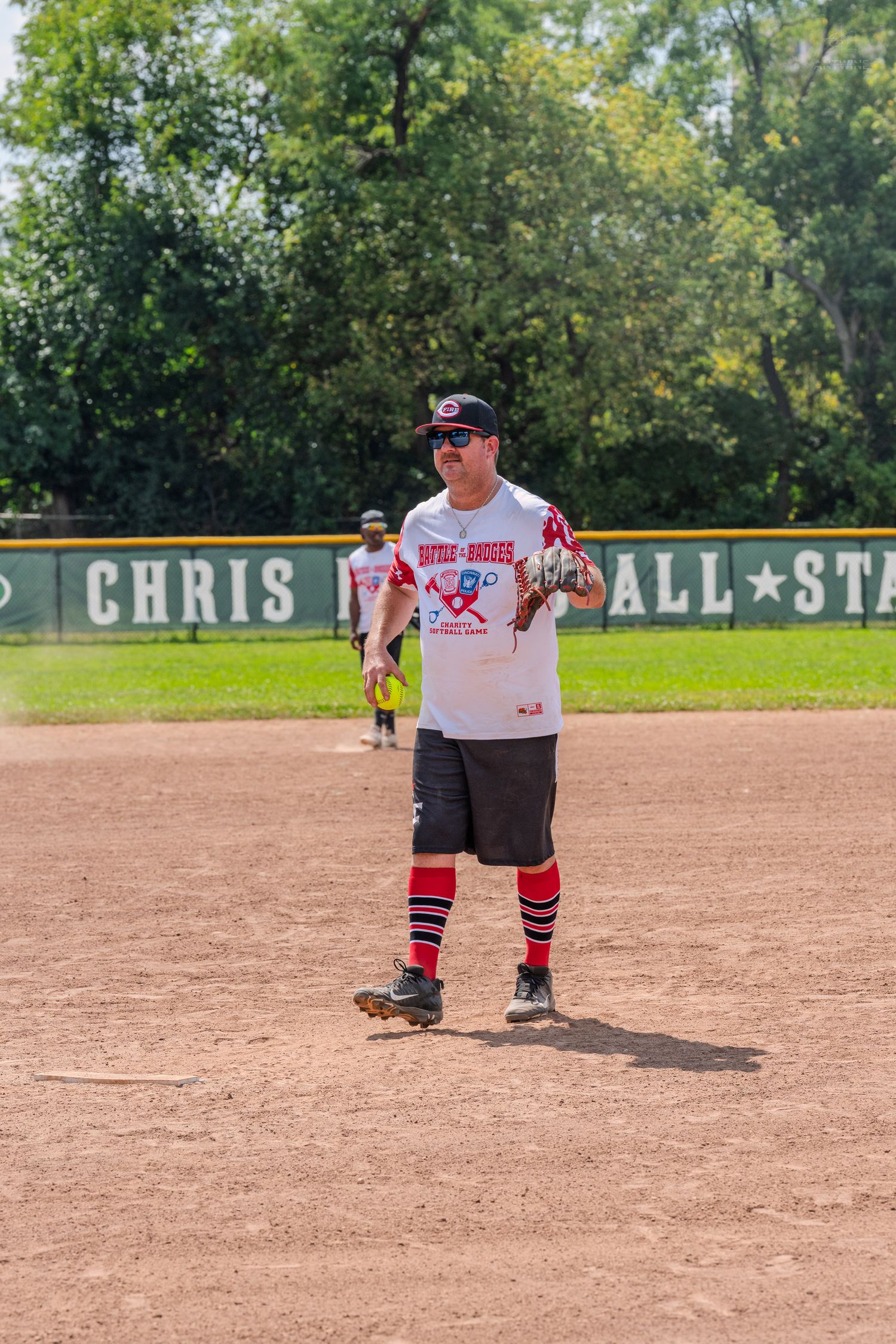 Softball player in red socks and white jersey holding a ball on the infield during a game.