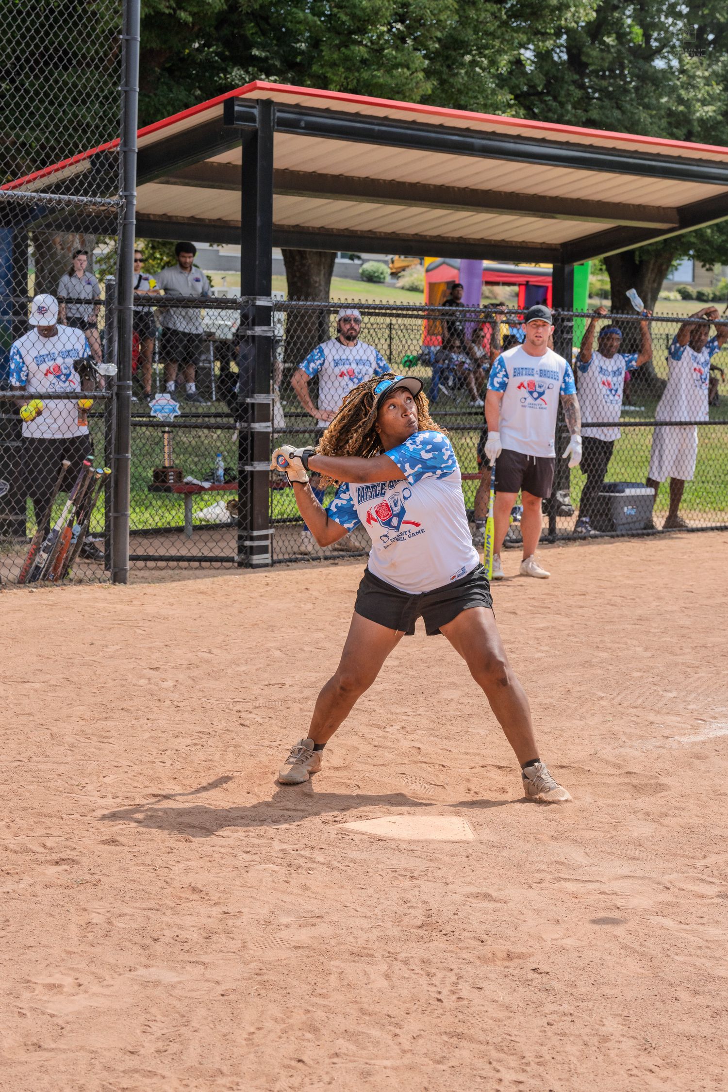 A female softball player with dreadlocks swings a bat at home plate during a game.