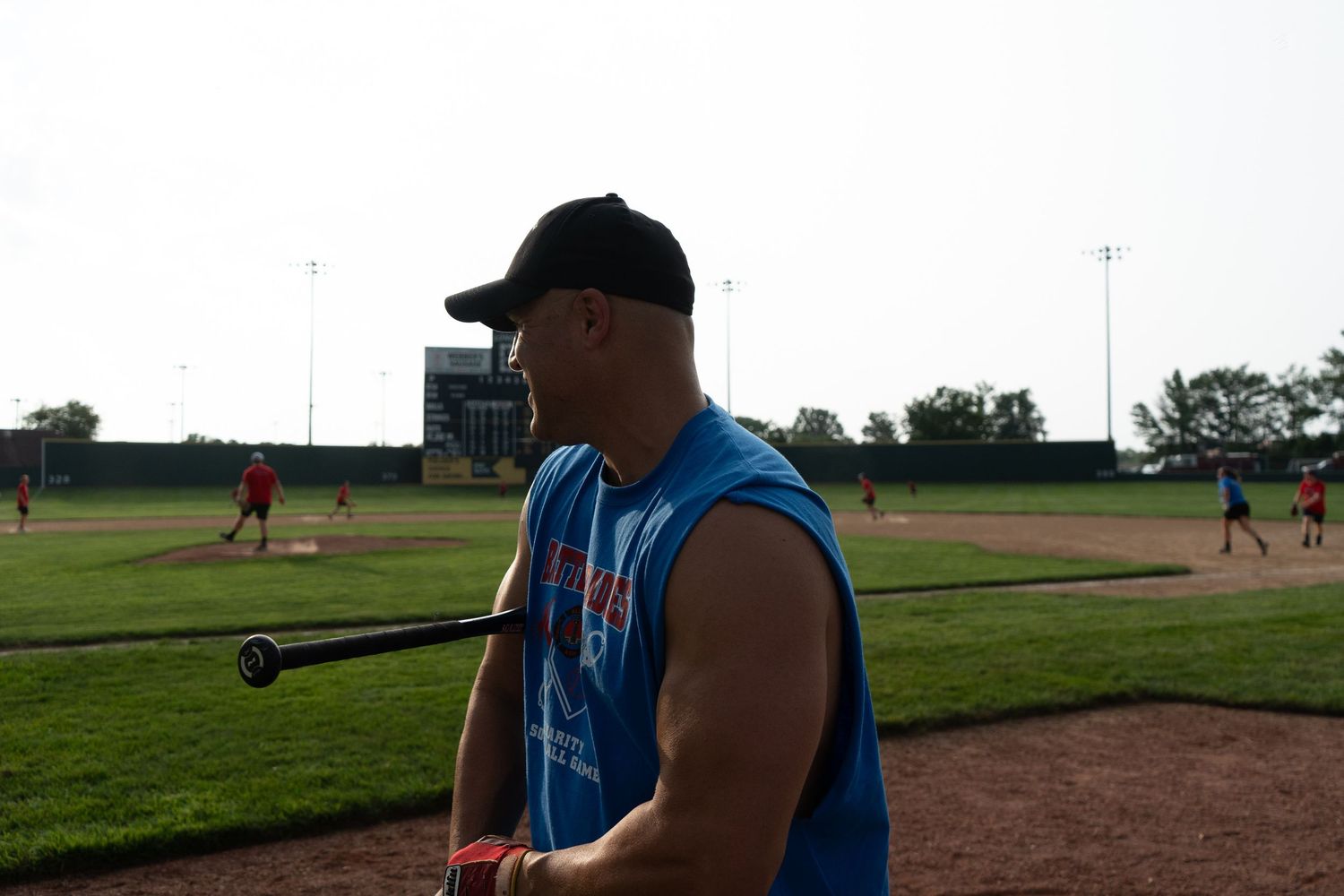 Muscular man in blue sleeveless shirt holding a bat at a baseball field during practice.