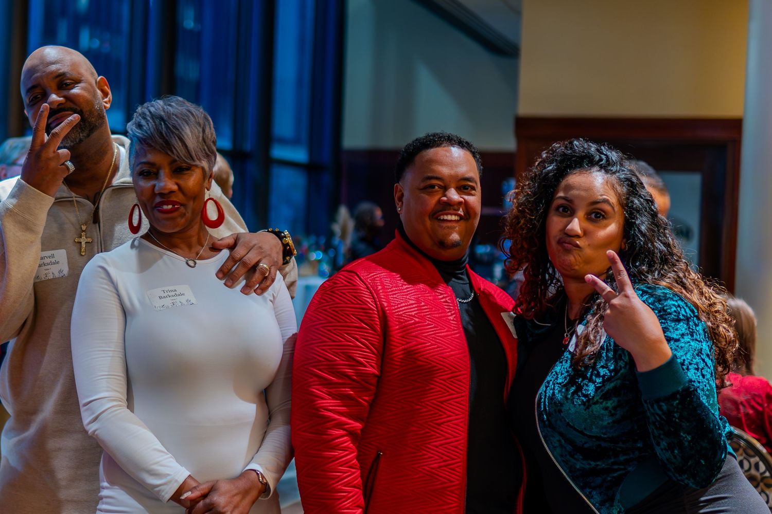 Four people smiling and posing together at a formal indoor event, dressed in elegant attire including red and teal outfits.