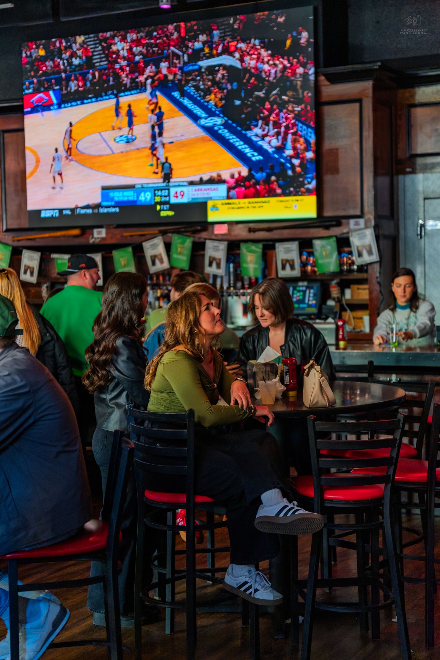 Women socializing at a sports bar with a basketball game on a large TV screen above them.