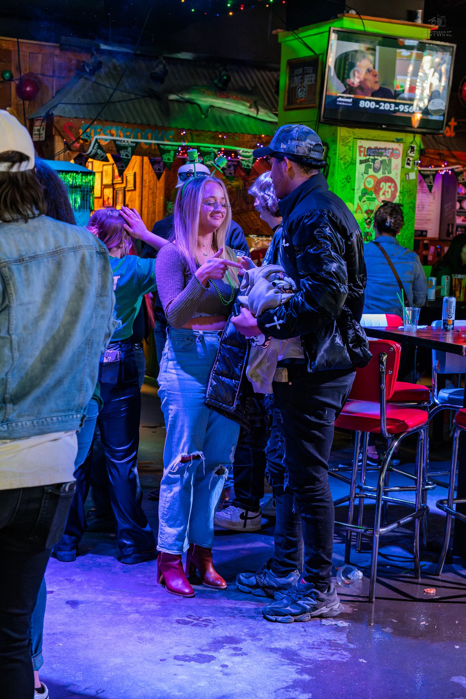 Couple dancing together in a lively bar with purple lighting, ripped jeans, and colorful decor.