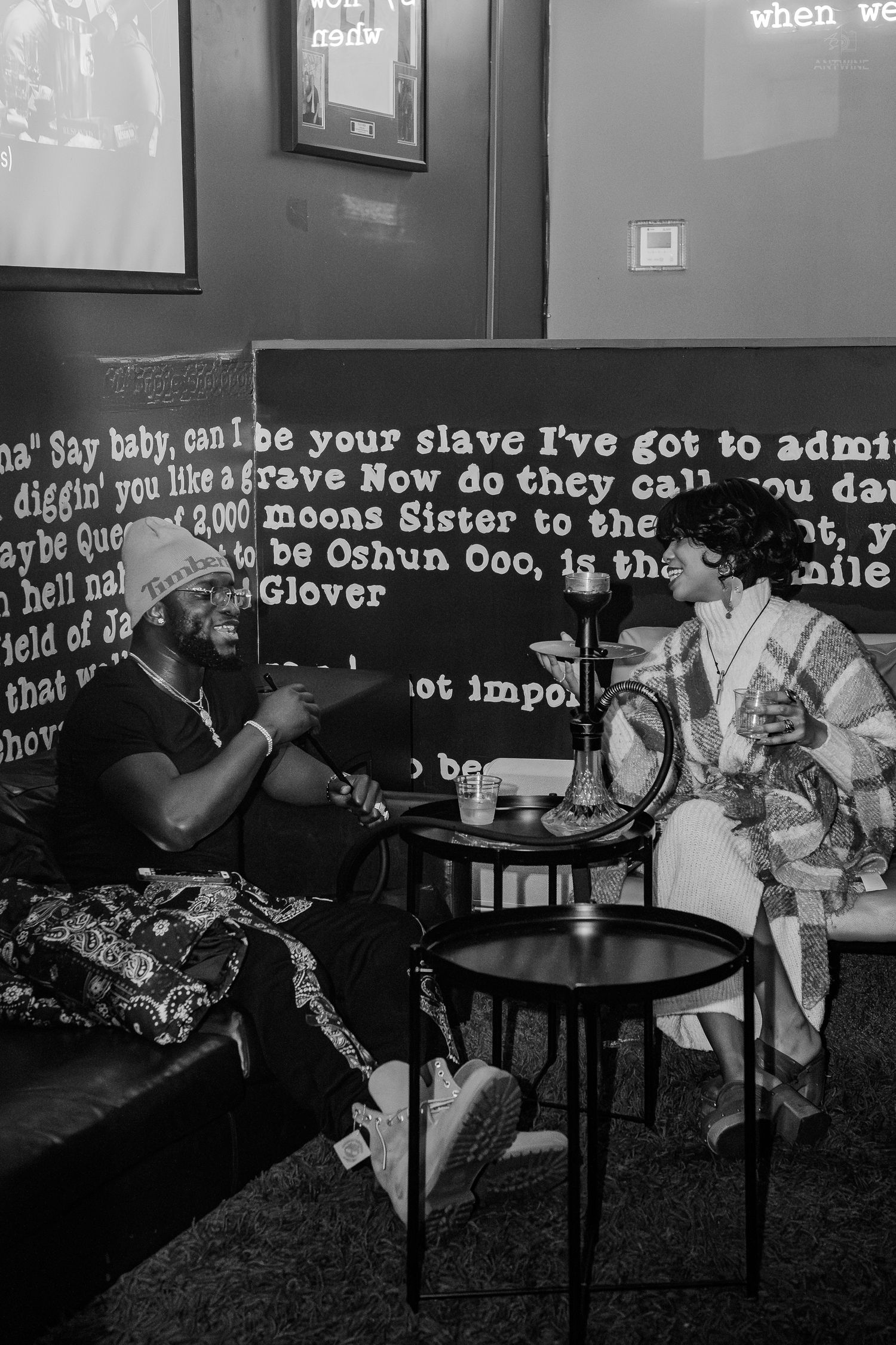 Two people in traditional attire converse in a stylish lounge with lyric-covered walls in black and white photo.