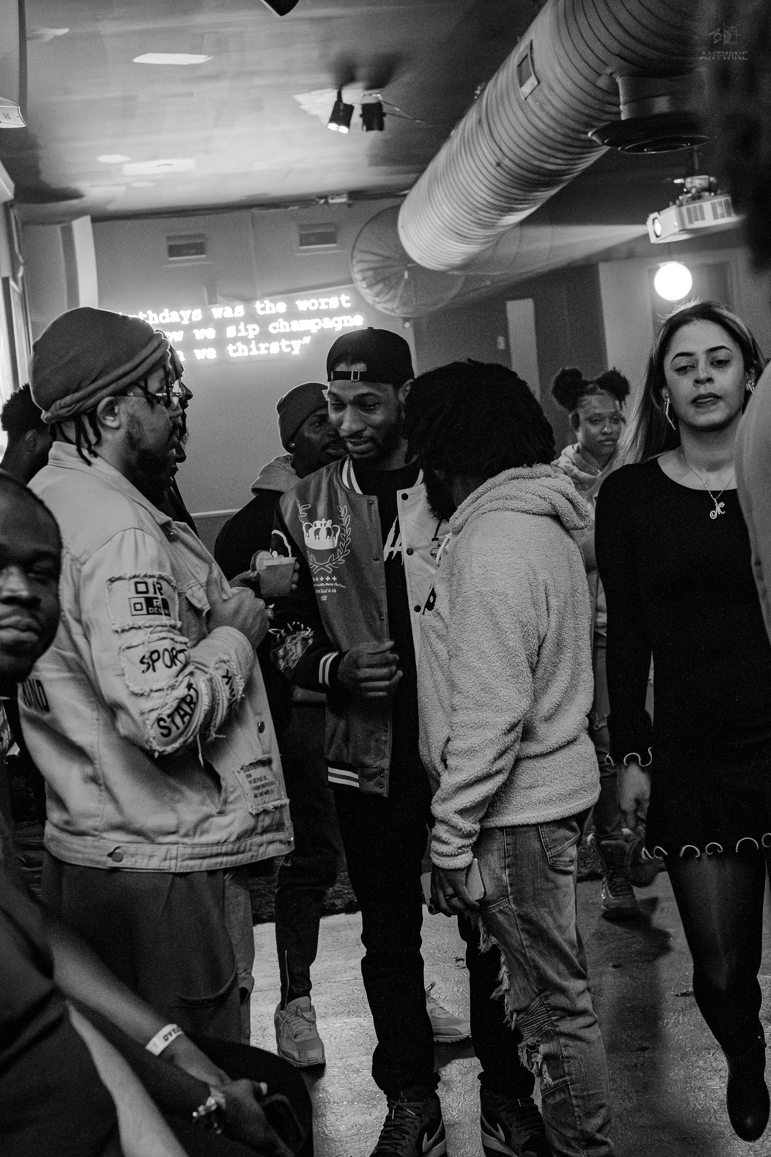 Black and white photo of a group of young people socializing at an indoor event or party.