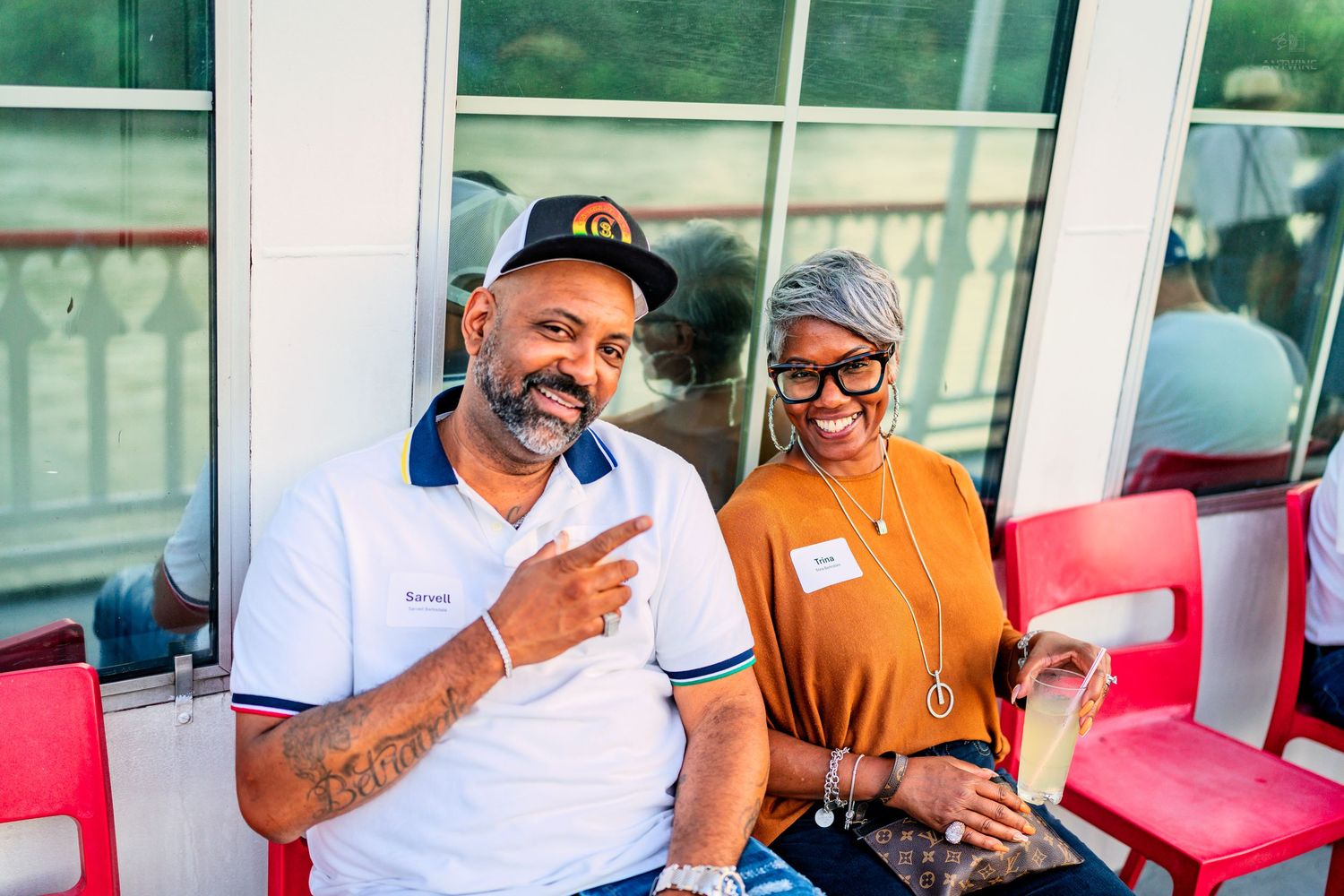 Two people smiling and posing together at an outdoor social event on a sunny day.