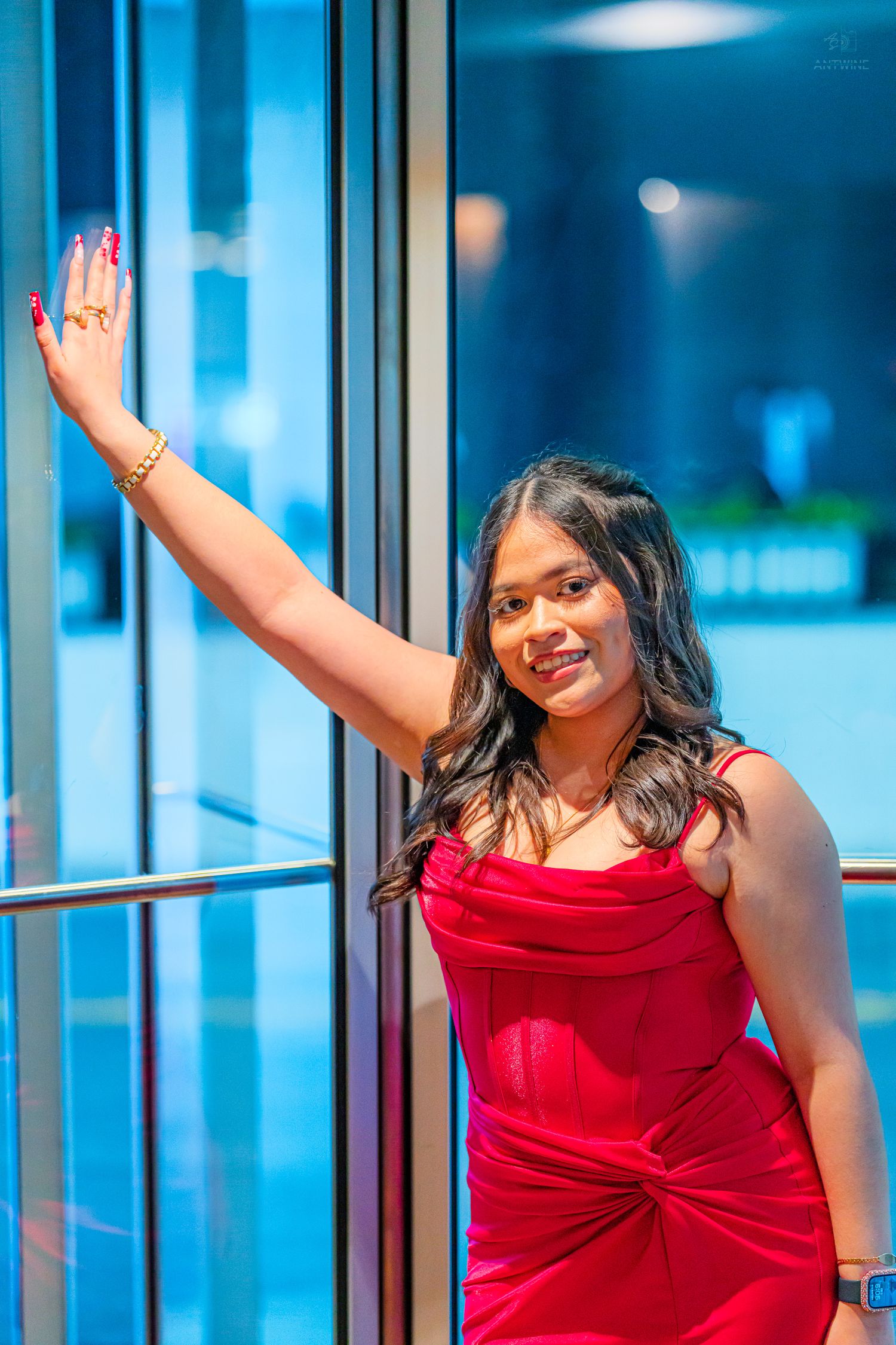 Smiling woman in red velvet dress posing by glass doors at formal event.