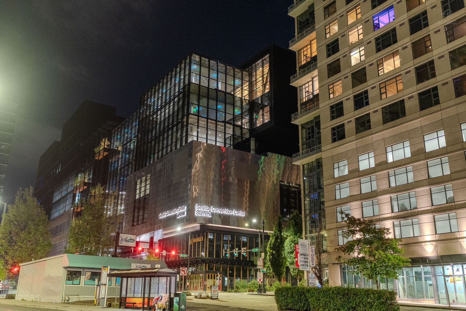 Modern urban buildings illuminated at night with glowing windows and street lights in a city landscape.