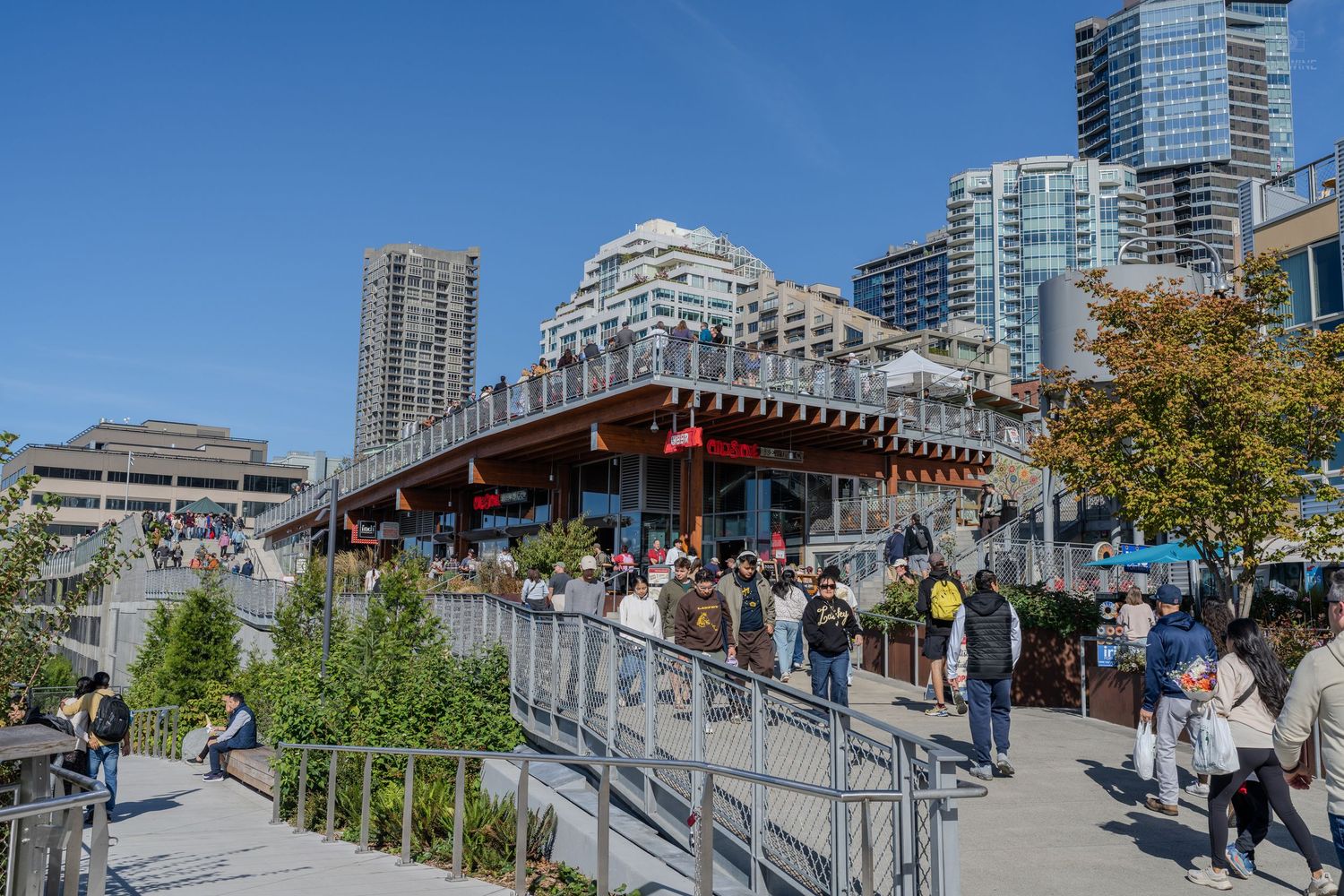 Visitors exploring a busy waterfront marketplace in Seattle with modern high-rise buildings in the background.