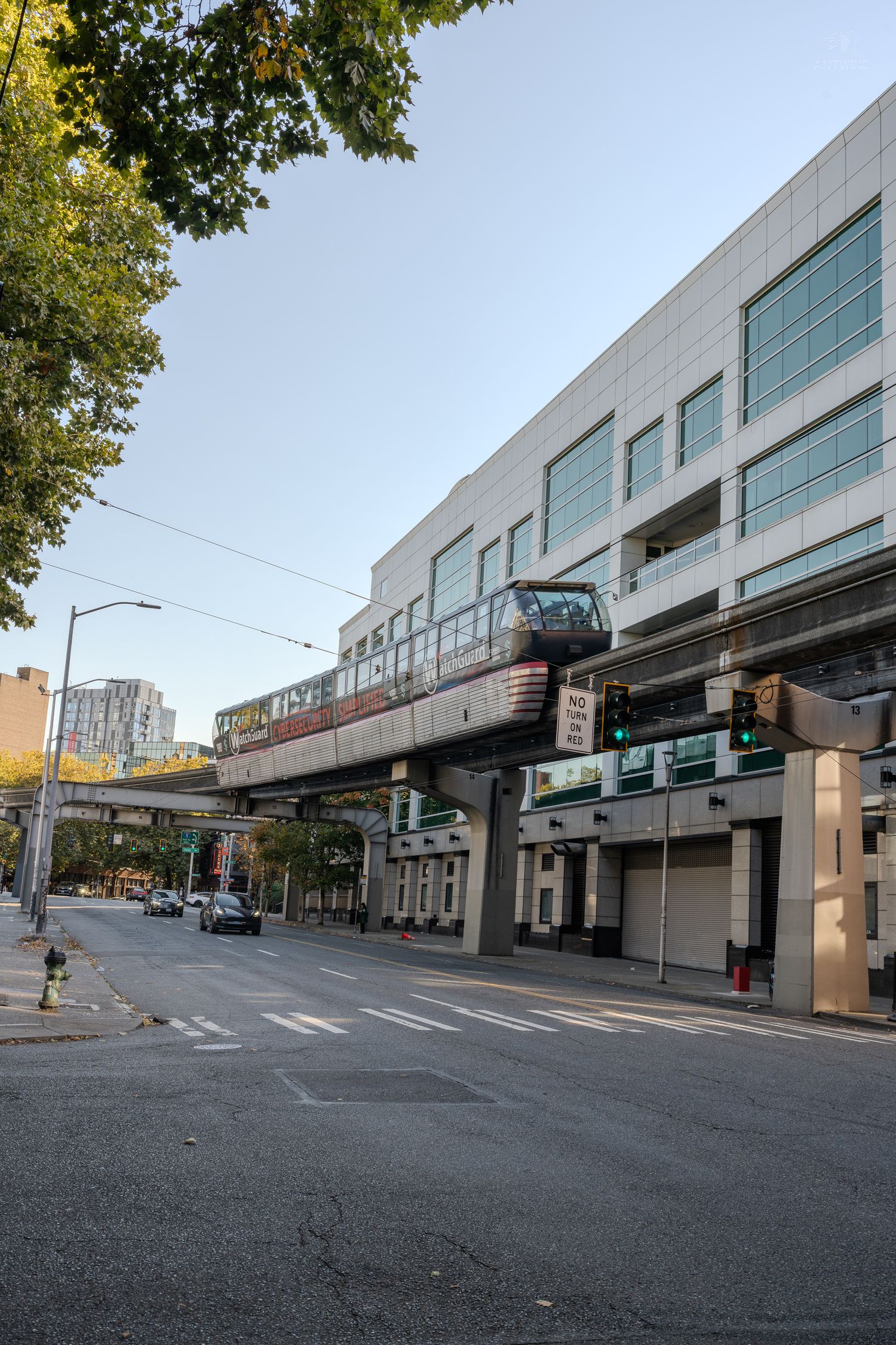 Seattle monorail train passing over a quiet urban street on a clear day.