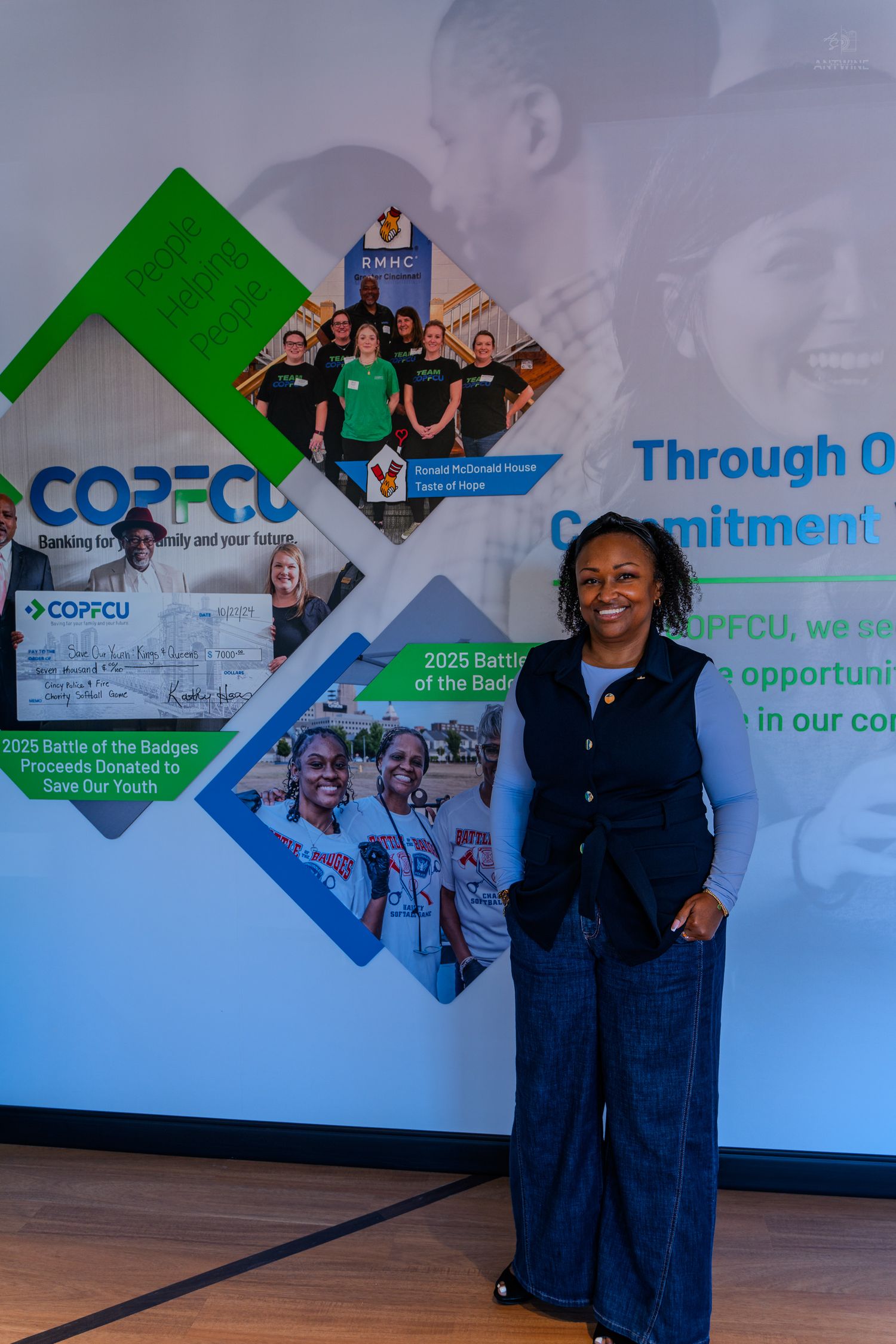 Woman smiling in front of COPFCU credit union promotional display highlighting community commitment and youth programs.