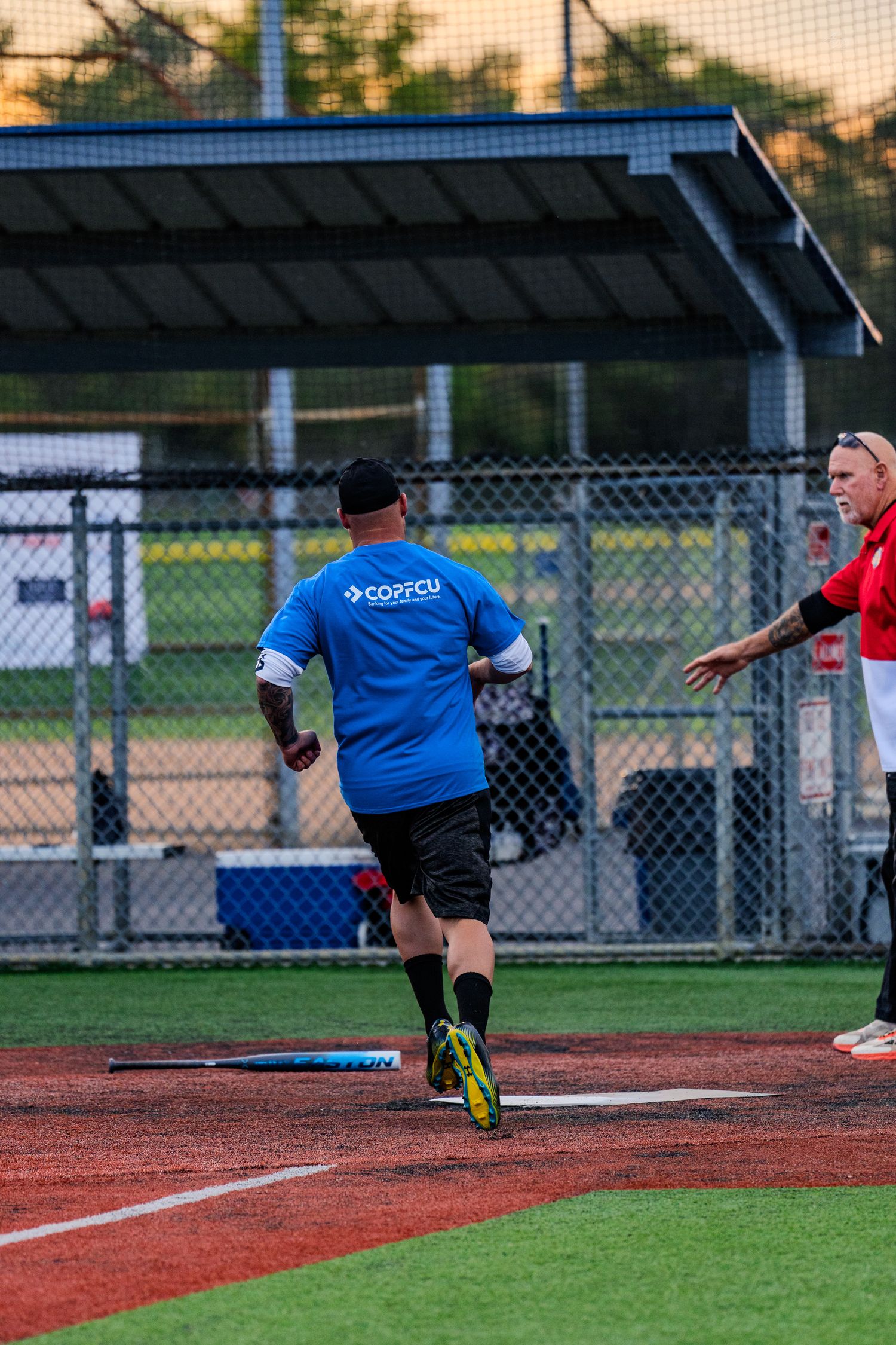 Softball player in blue COPFCU jersey running bases during an evening recreational league game.