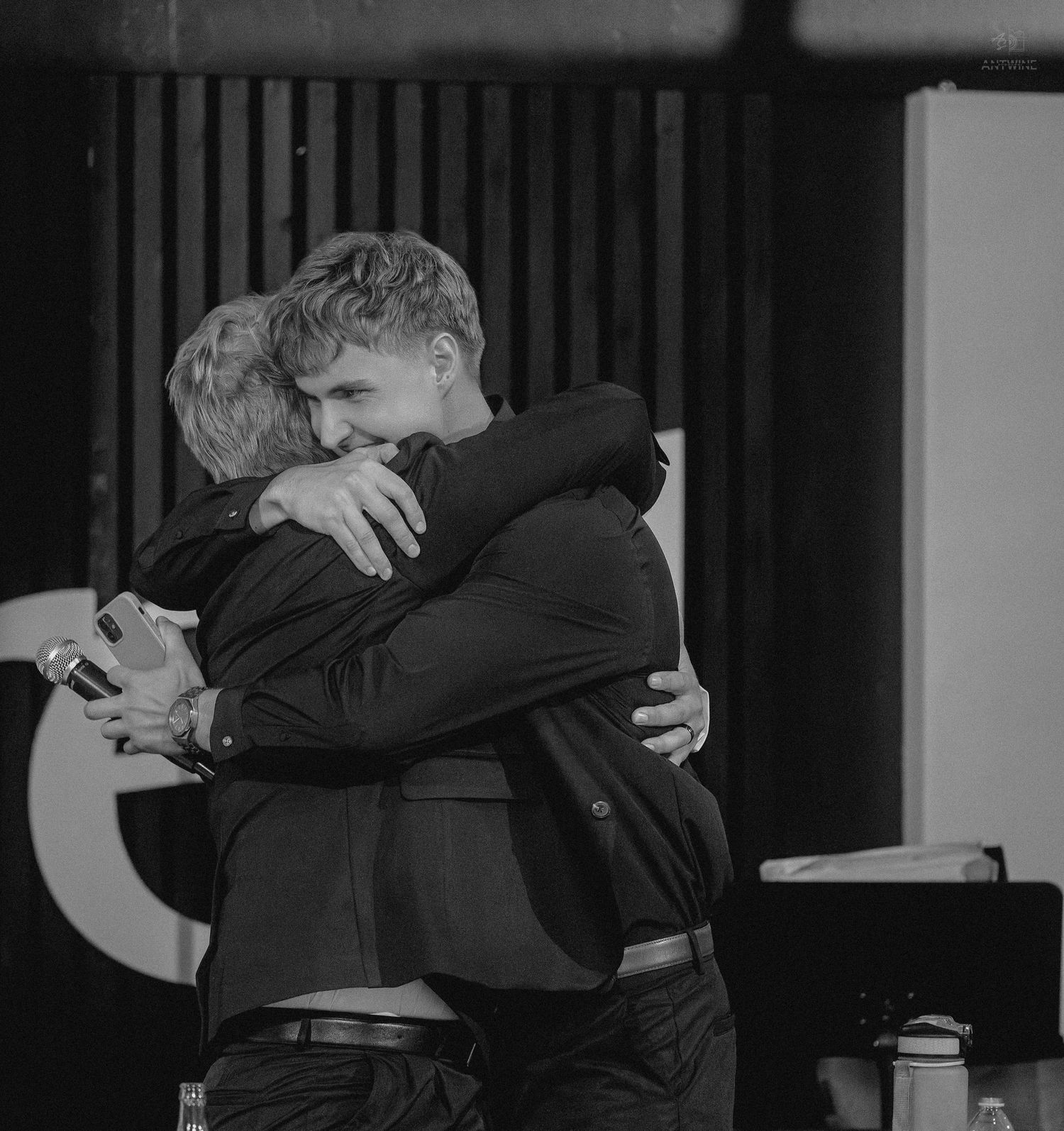 Two young men share a heartfelt embrace in a tender black and white wedding reception photo.