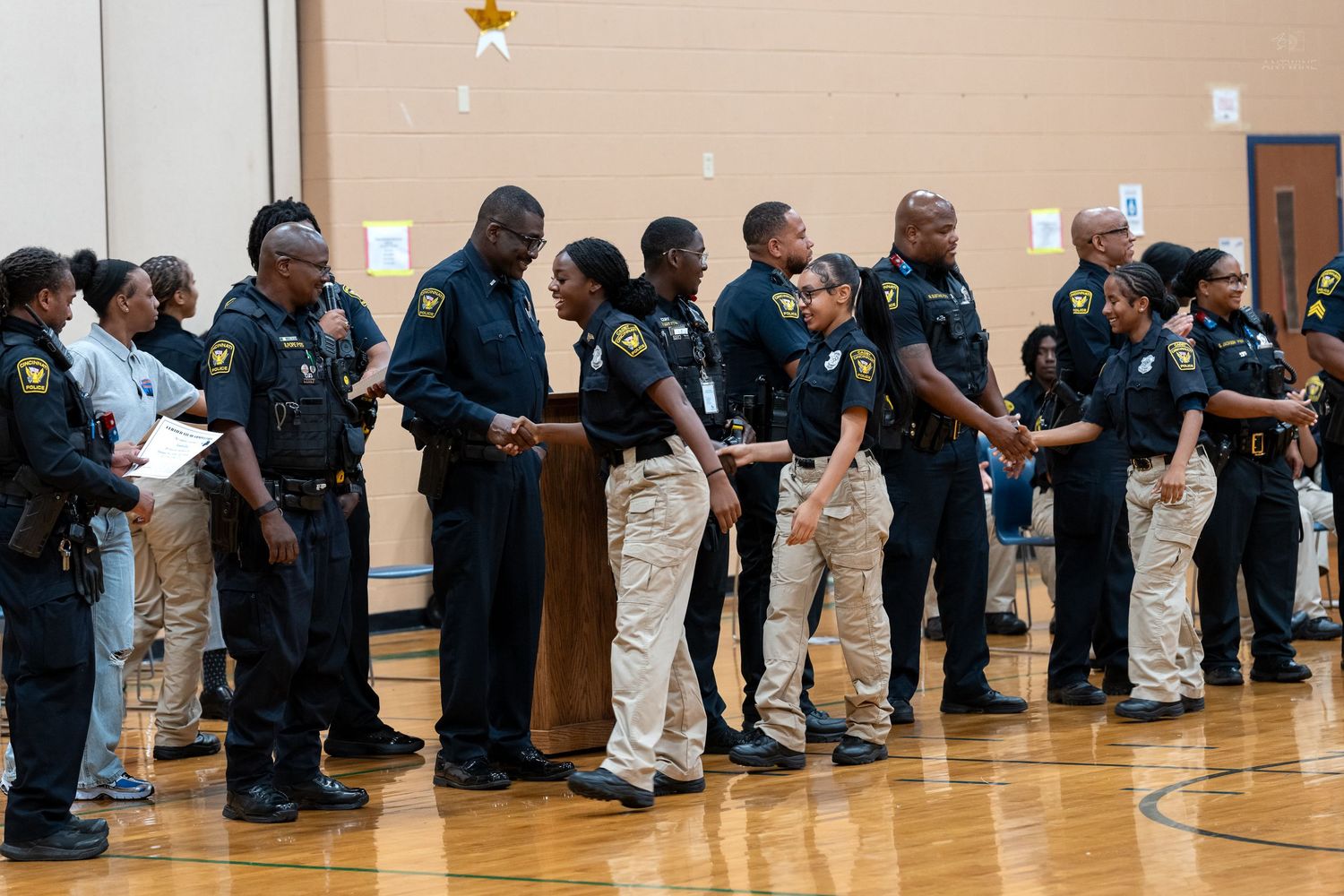 A group of Black police officers in uniform form a long line during an official ceremony indoors.