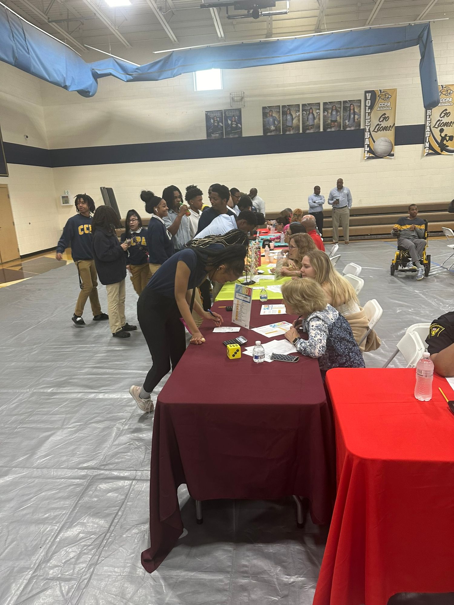 Students and staff gather at tables in a school gymnasium during a career fair or registration event.