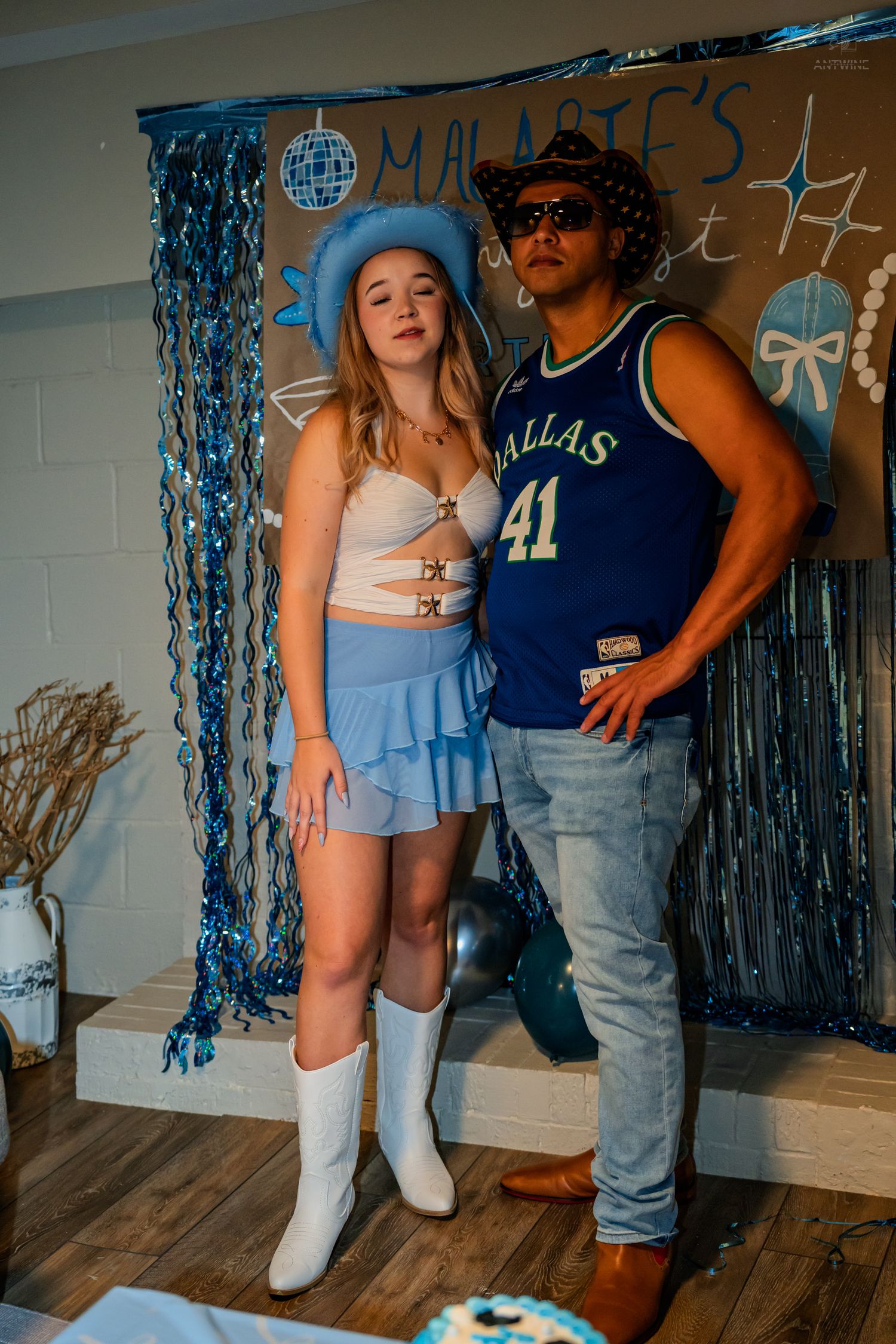 Young woman in blue skirt and white boots poses with man at birthday party.