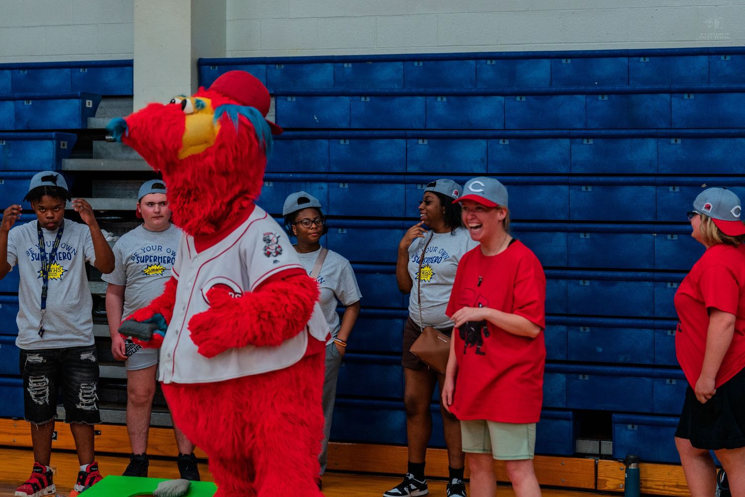 Cincinnati Reds mascot Mr. Red interacts with youth participants in red shirts inside a gymnasium.