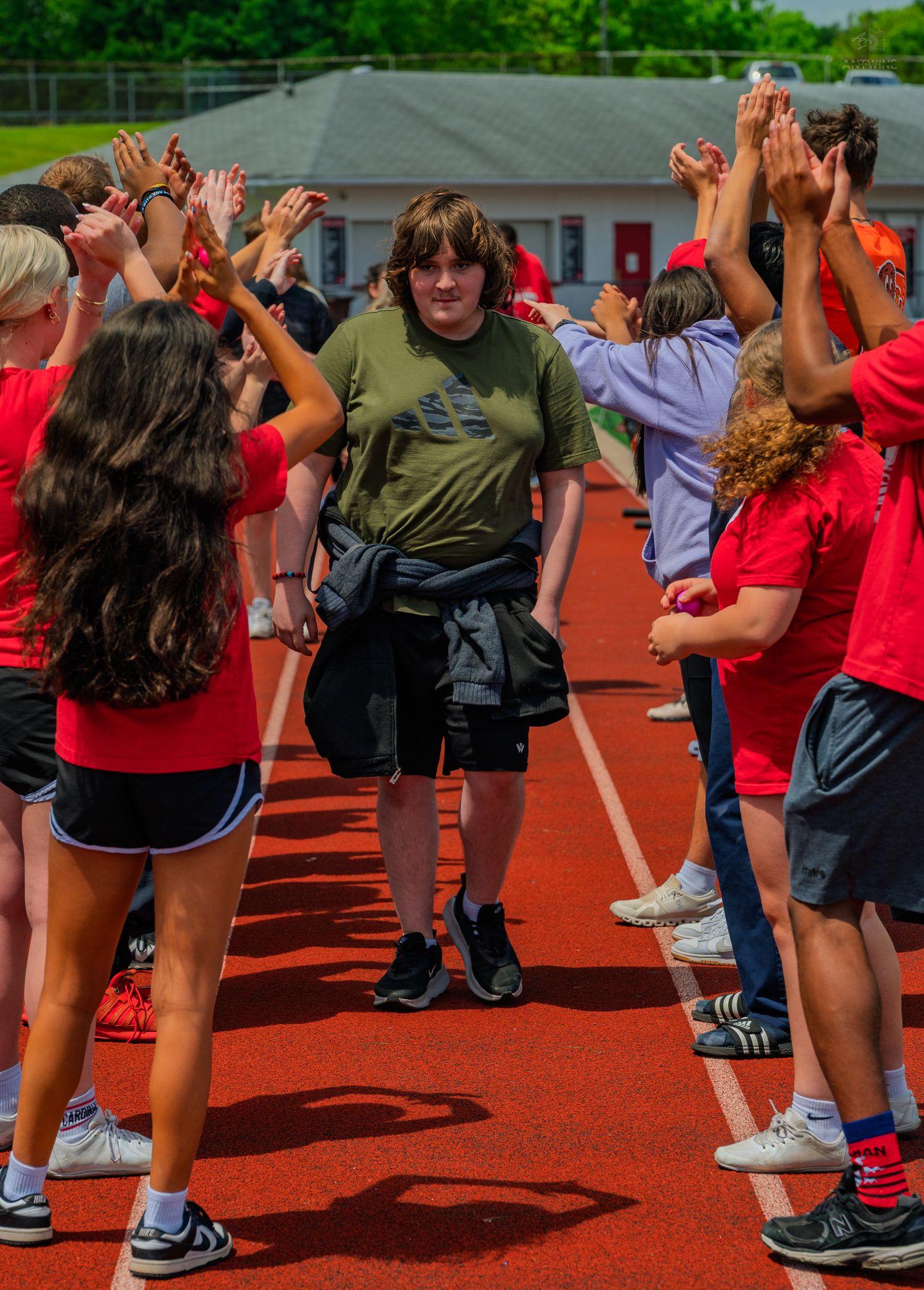 Student walks through a celebratory high-five tunnel formed by peers in red shirts on a school running track.