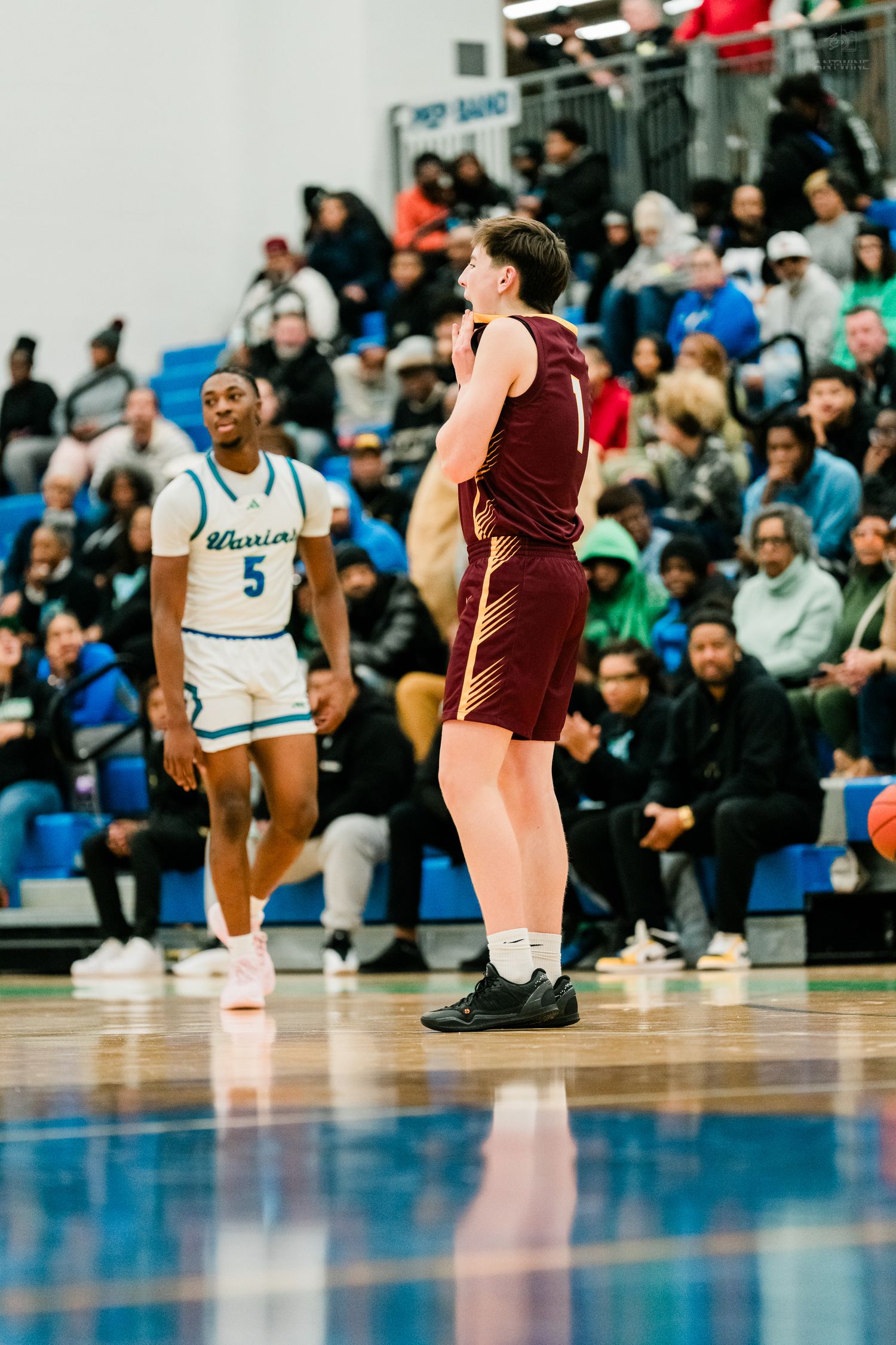 A maroon-uniformed basketball player stands on court as a Warriors player in white jersey number 5 looks on.