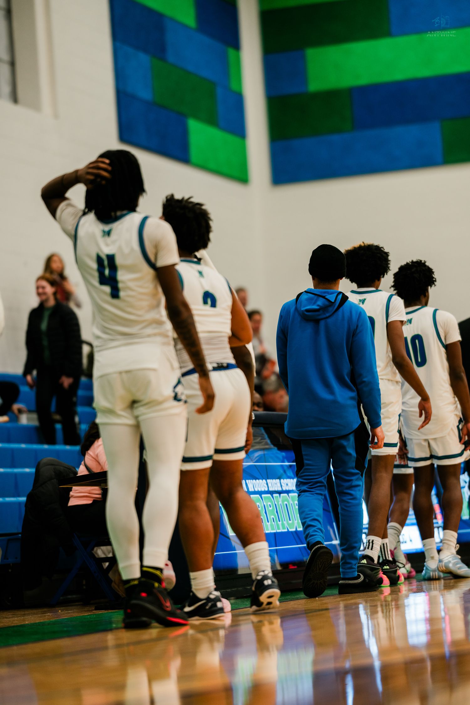 Warriors basketball players stand near the bench with one player holding his head during a high school game.